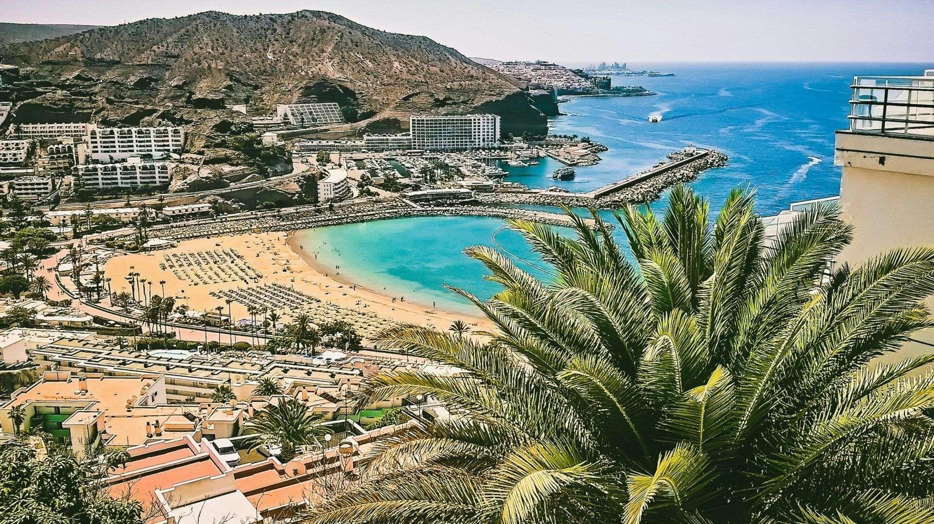 Vista panoramica di una spiaggia con hotel, montagne rocciose, acqua turchese e palme tropicali