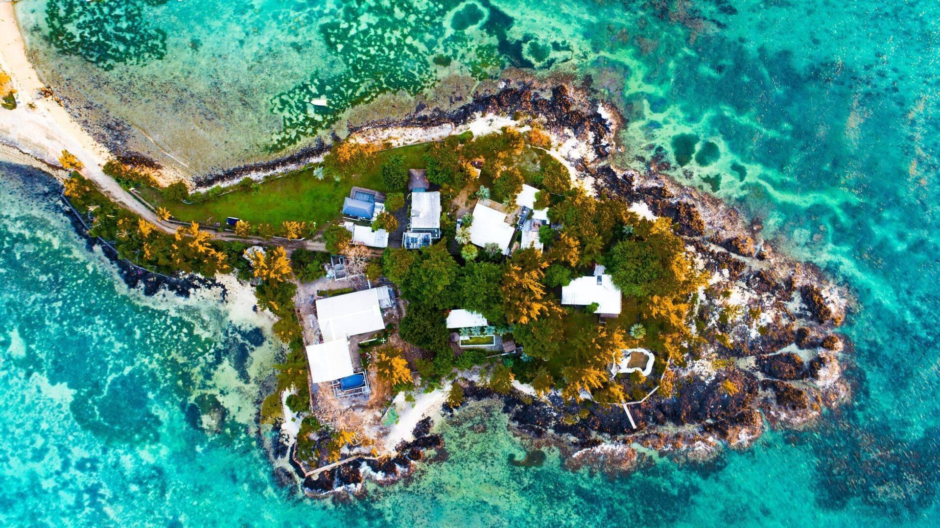 Luftaufnahme einer kleinen Felseninsel mit weißen Häusern, grüner Vegetation und kristallklarem türkisem Wasser