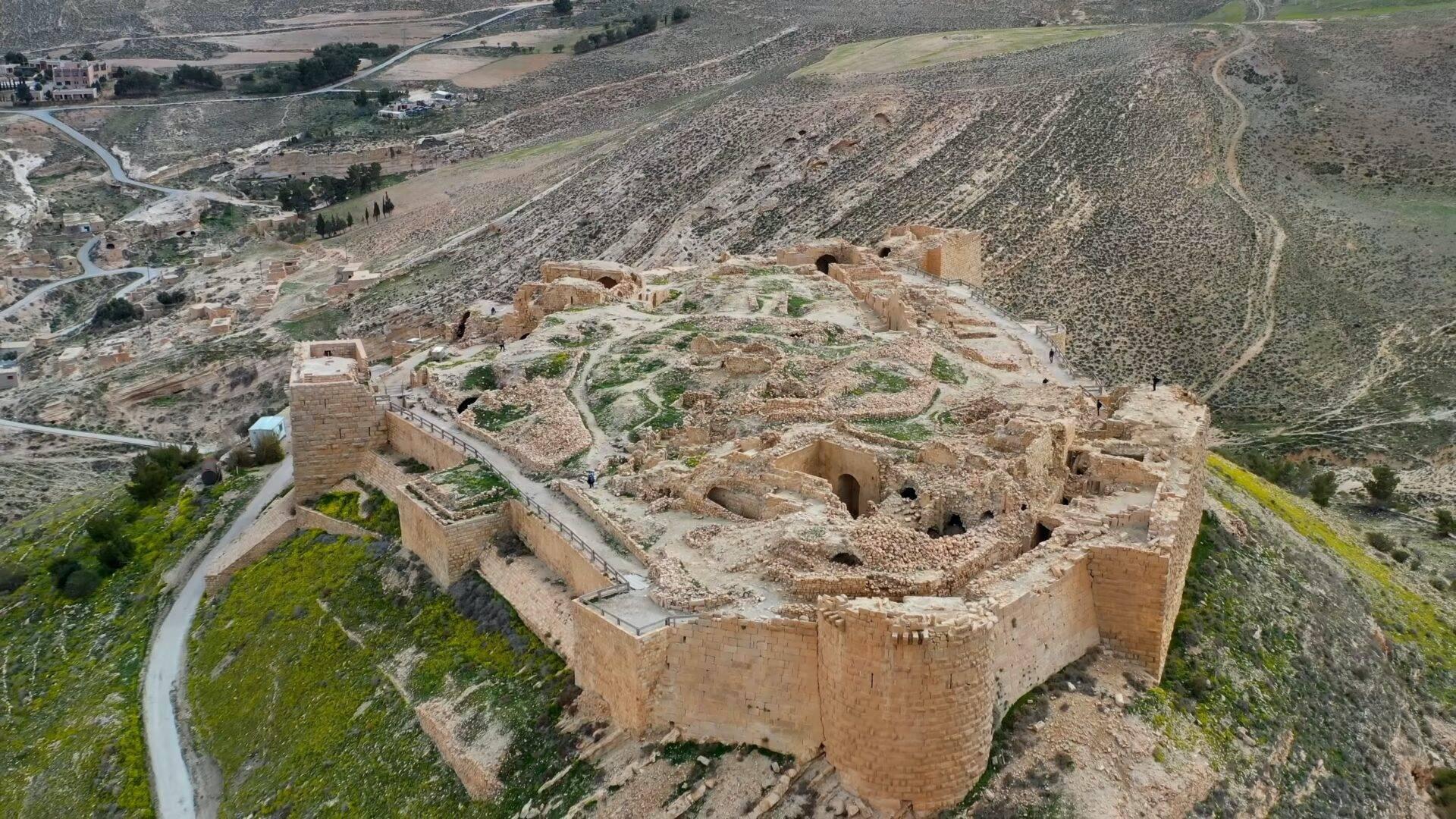 Fortezza in rovina vista dall’alto con mura in pietra che dominano un paesaggio montuoso arido e una valle verdeggiante sullo sfondo
