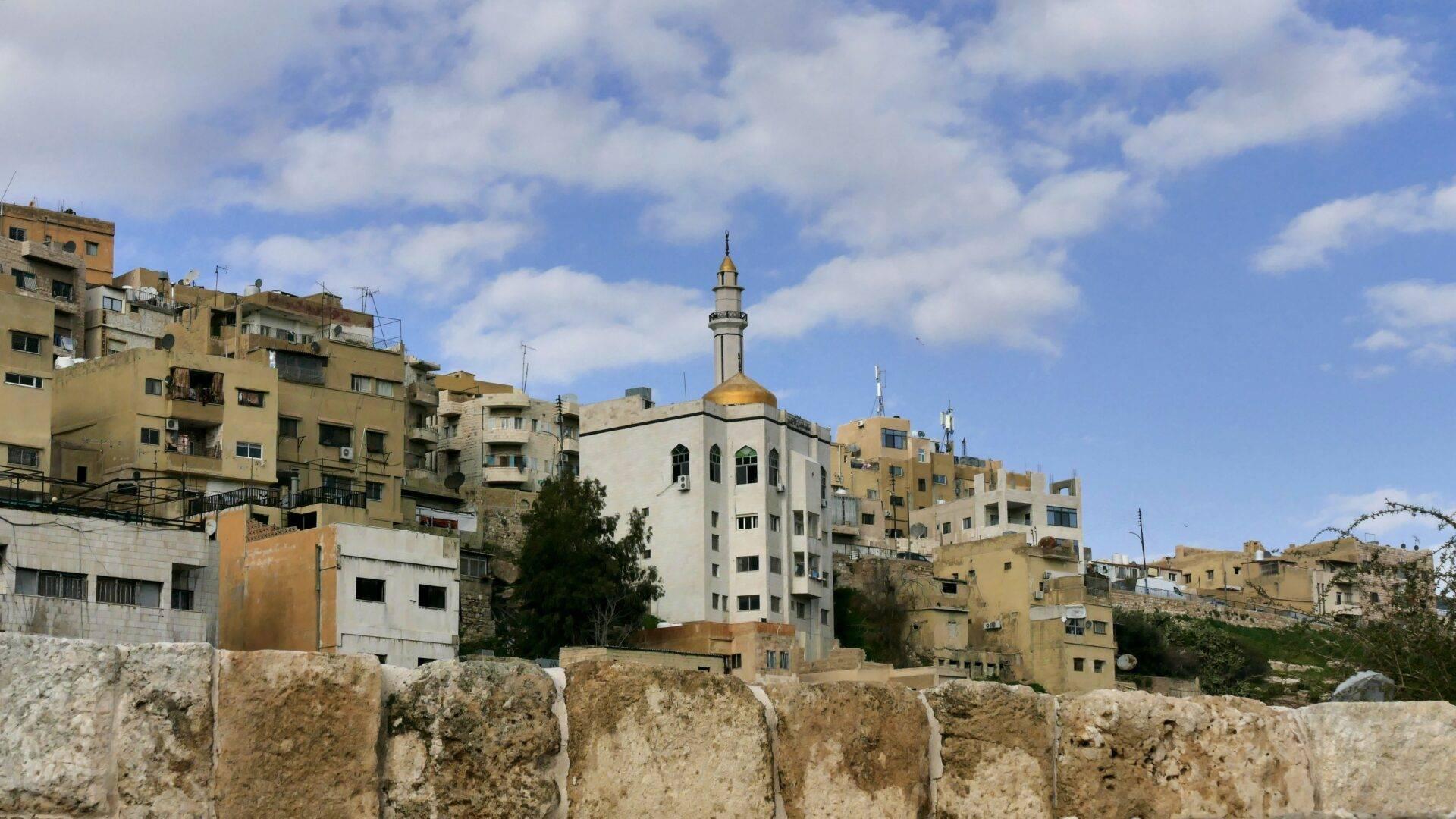 Vista di una città mediorientale con moschea a cupola dorata circondata da edifici in pietra beige e mura di cinta