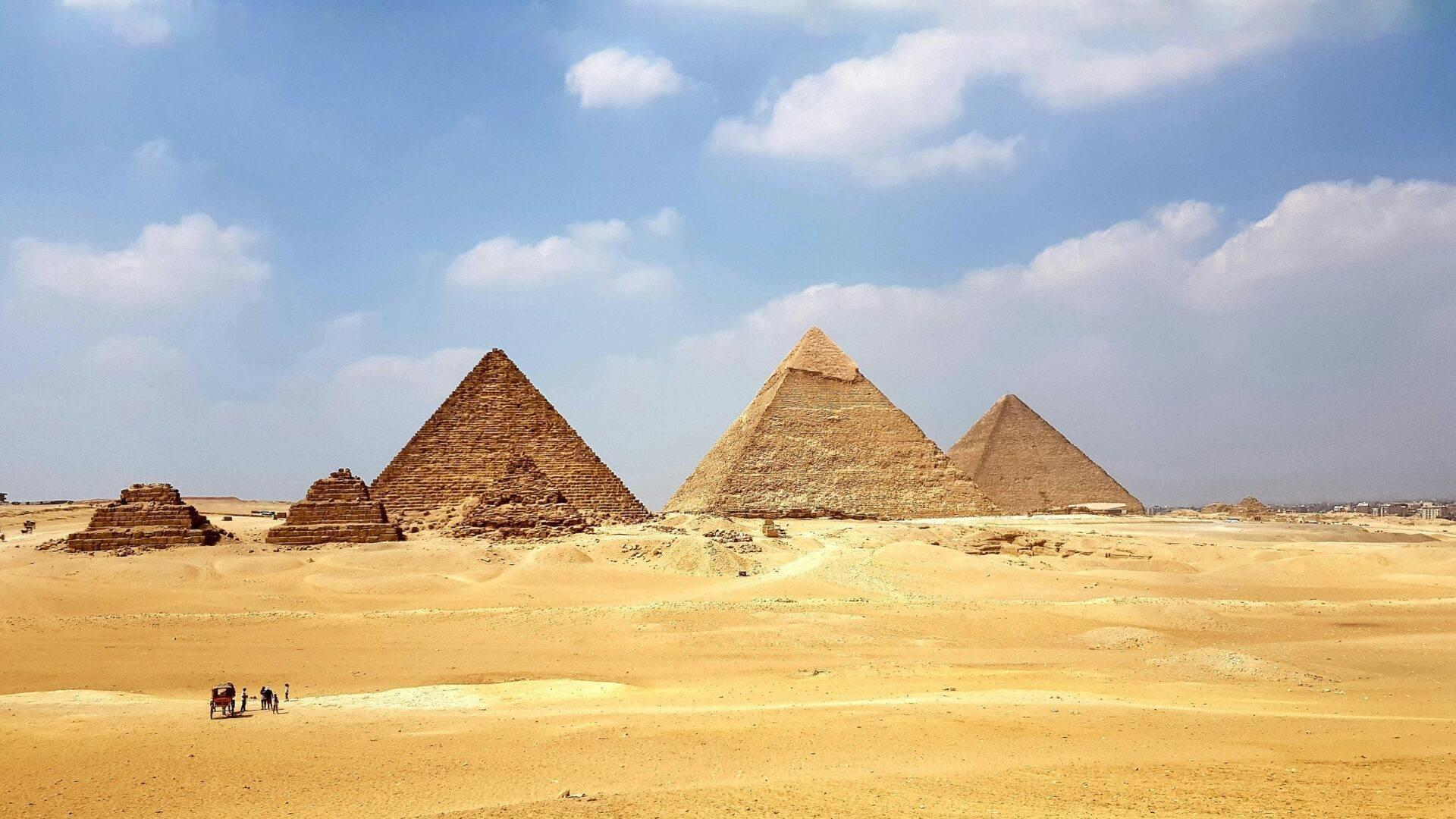 Trois pyramides de pierre dans un désert aride sous un ciel bleu dégagé avec quelques visiteurs