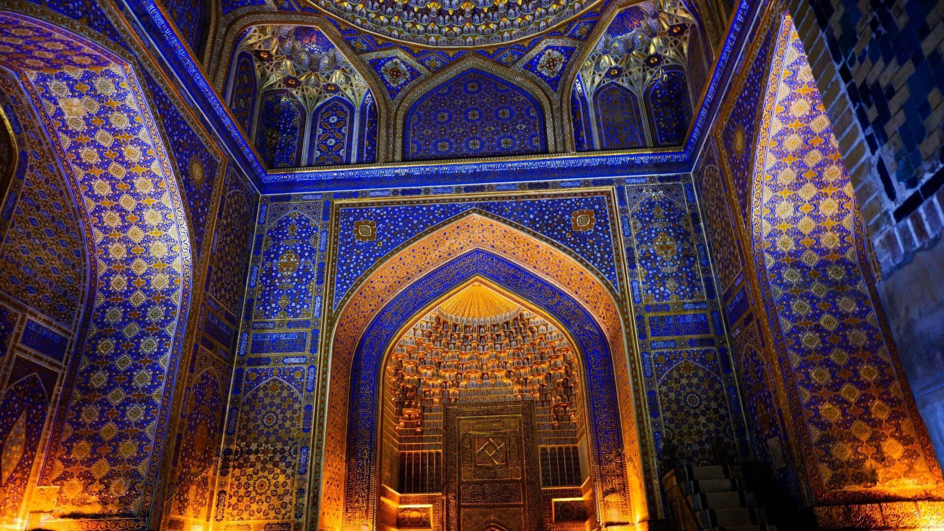 Intérieur richement décoré d’une mosquée avec murs bleu cobalt, ornements dorés et porte monumentale illuminée