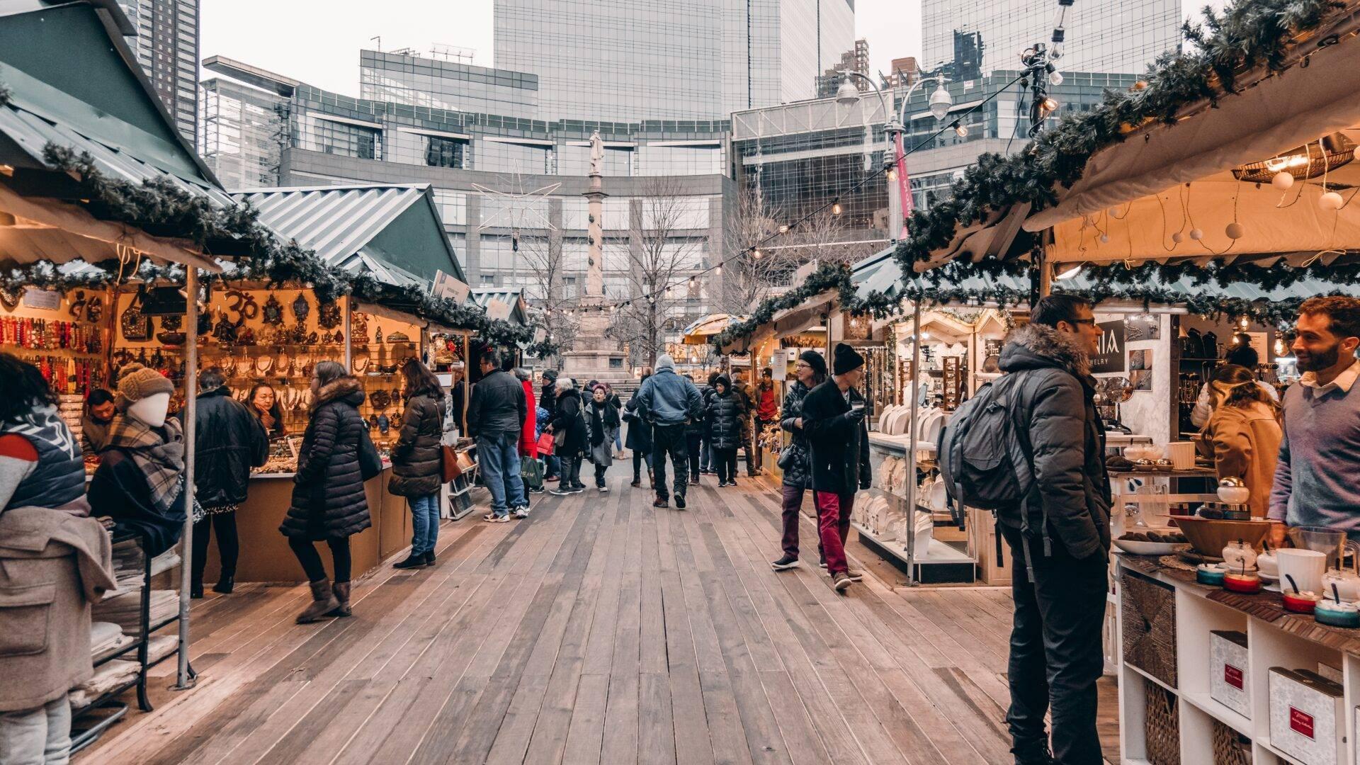 Un marché de Noël en plein air avec des petits chalets décorés de guirlandes, dans une cour urbaine entourée de gratte-ciel