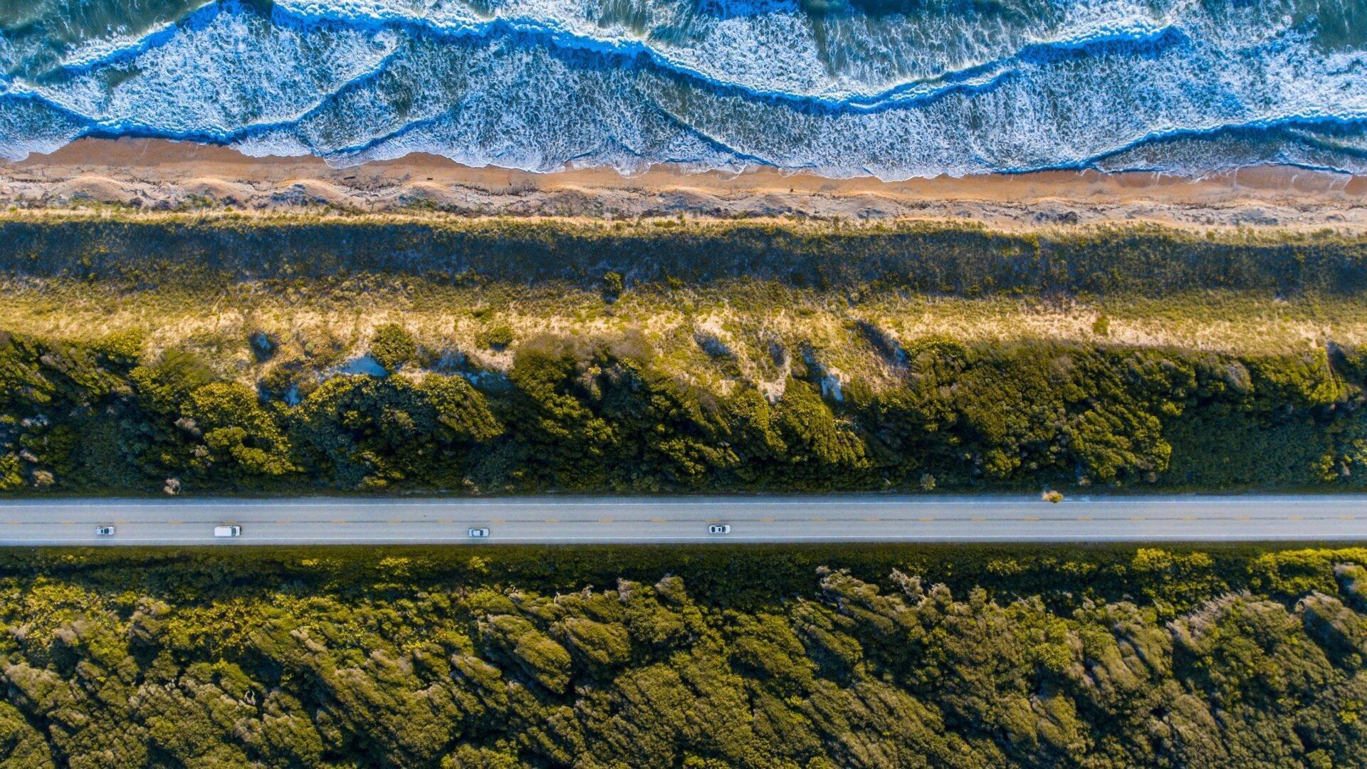 Luftaufnahme einer Küstenstraße durch üppigen Wald mit Strand und Wellen des Indischen Ozeans