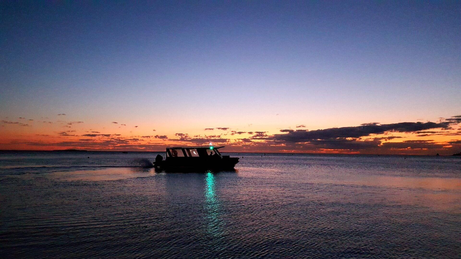 Un bateau à moteur silhouetté au coucher de soleil sur une mer calme et tranquille