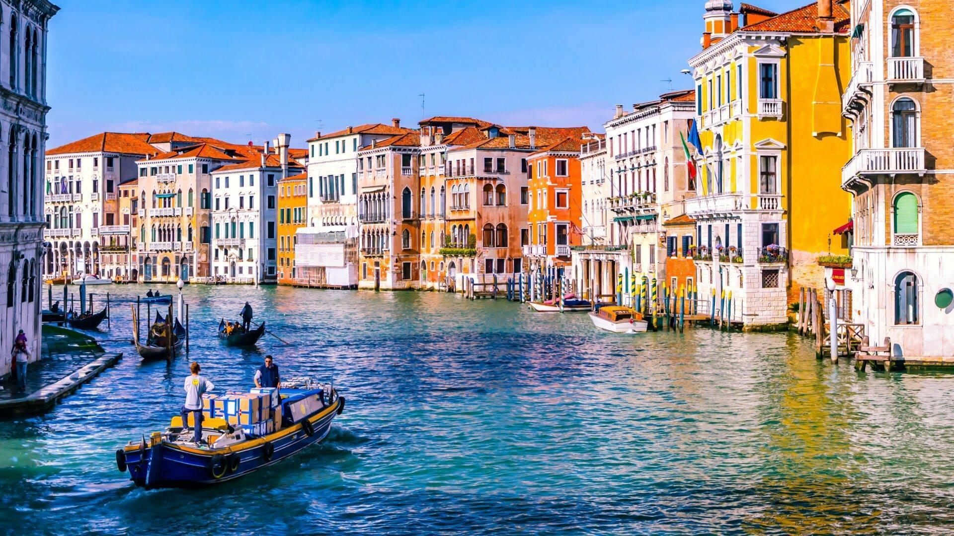 Vista panoramica del Canal Grande con i suoi edifici colorati, gondole e acqua azzurra sotto un cielo terso