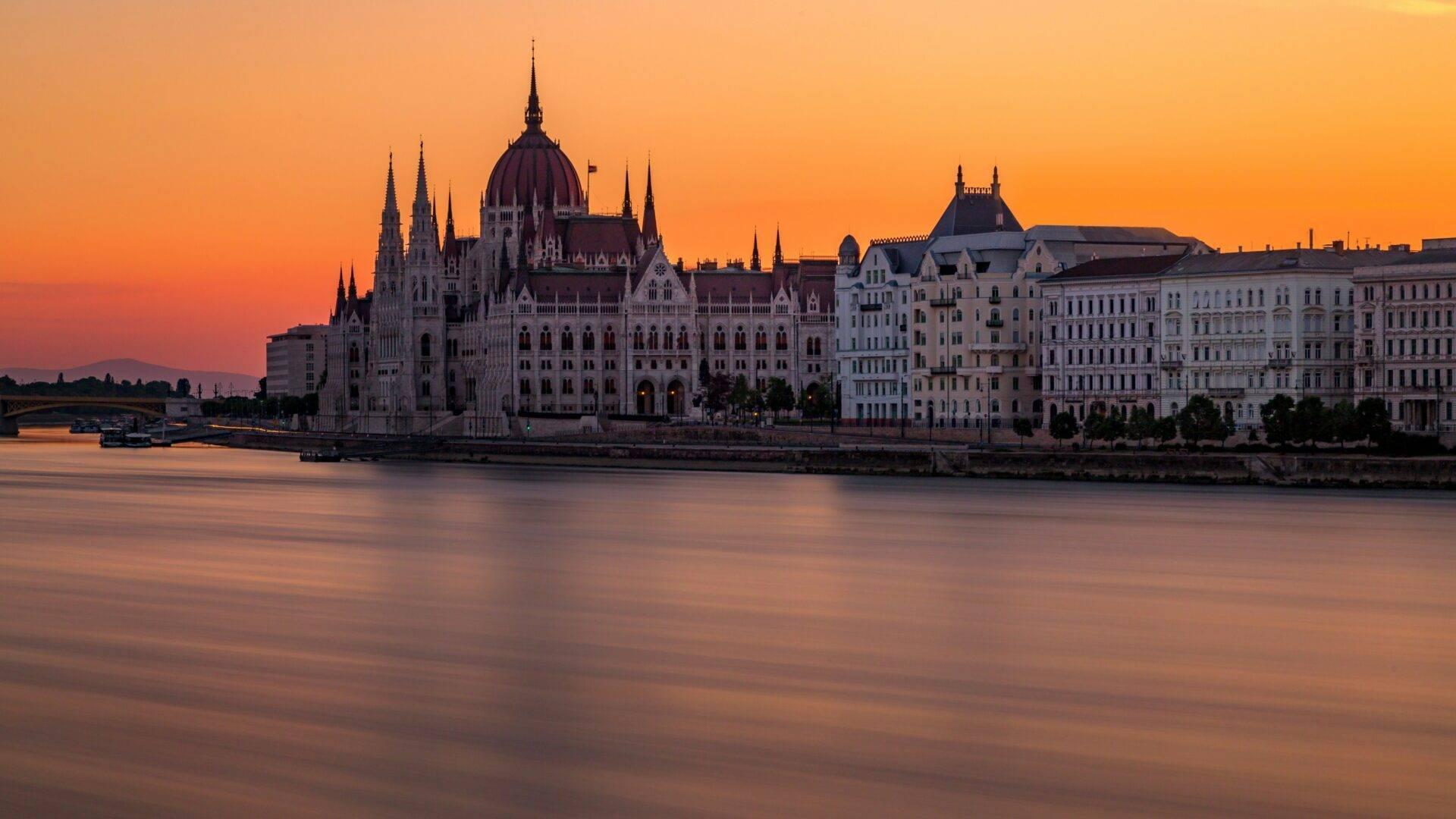 Imponente edificio gotico con cupola centrale e guglie appuntite in riva a un fiume al tramonto