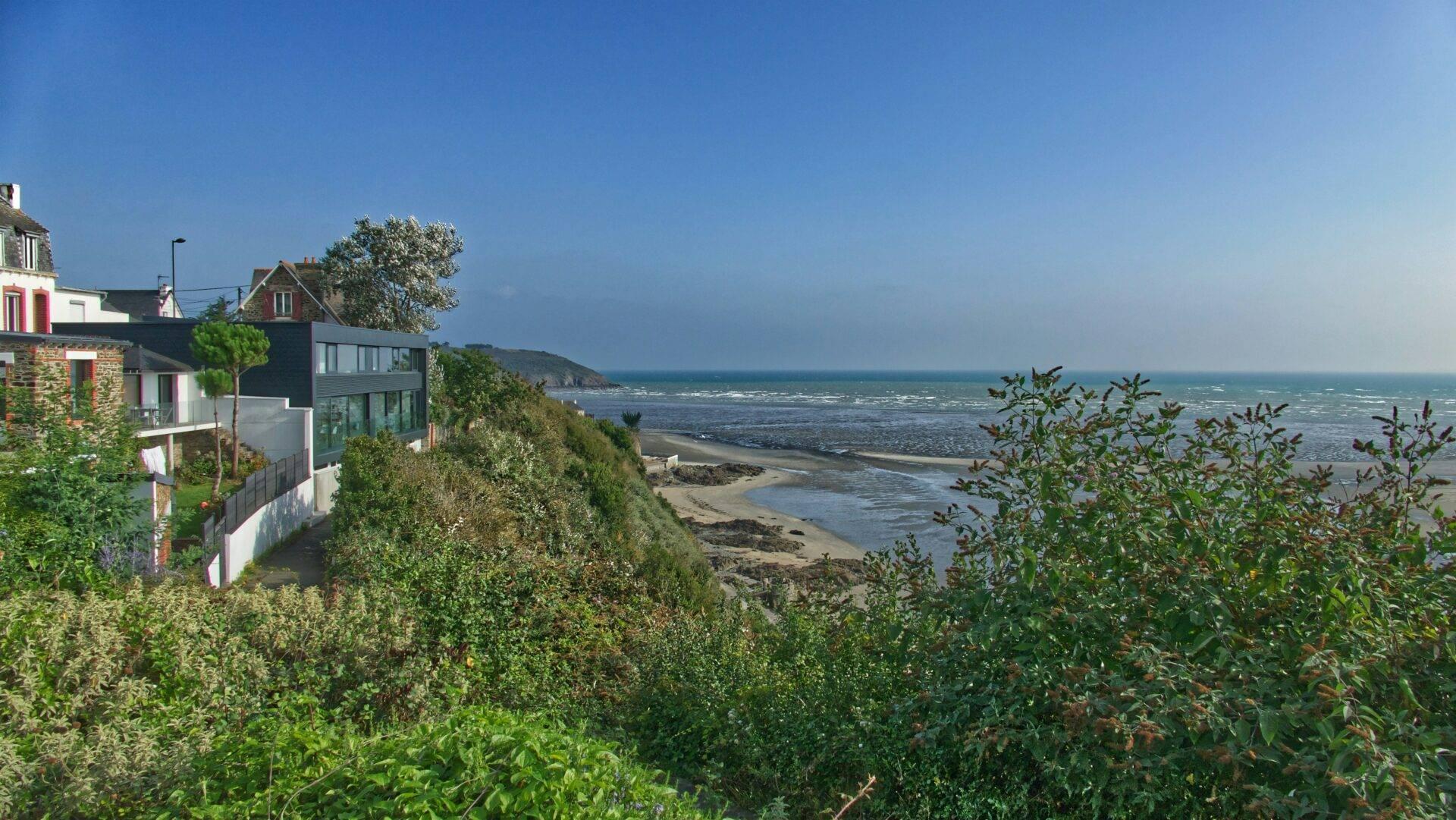 Case costiere moderne e tradizionali che si affacciano su una spiaggia rocciosa e il mare sotto un cielo azzurro limpido