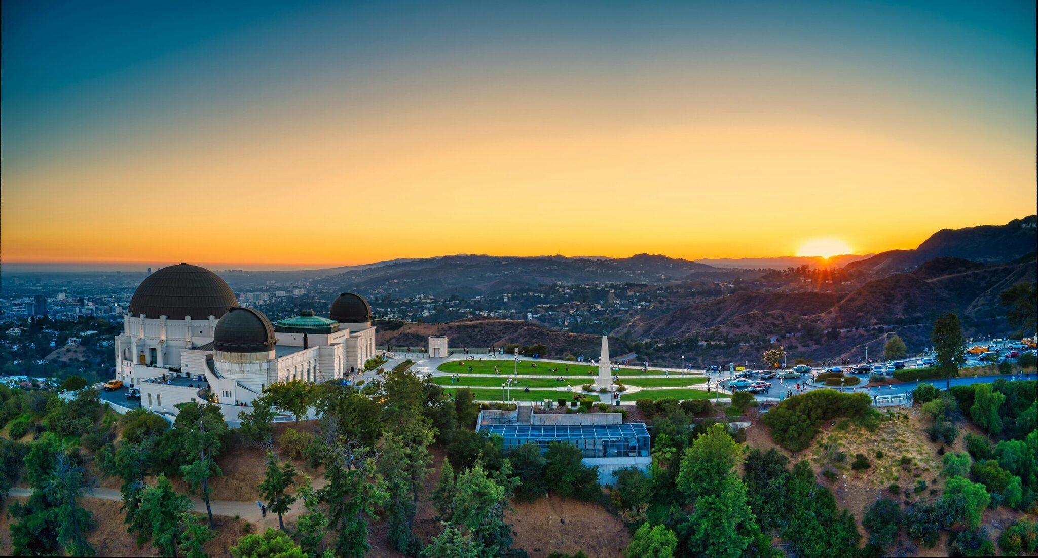 Das Griffith Observatory bei Sonnenuntergang hoch über Los Angeles mit seinen weißen Kuppeln und dem weit ausgedehnten Stadtpanorama darunter