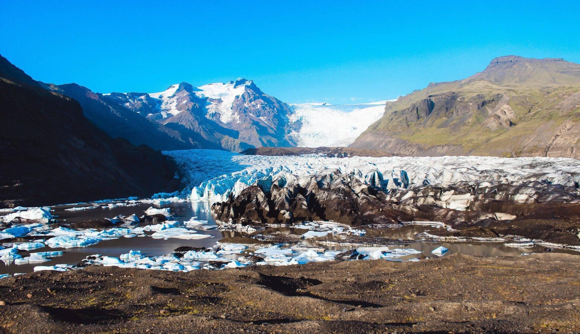 Un ghiacciaio bianco e blu incorniciato da montagne rocciose con blocchi di ghiaccio che galleggiano in un lago glaciale
