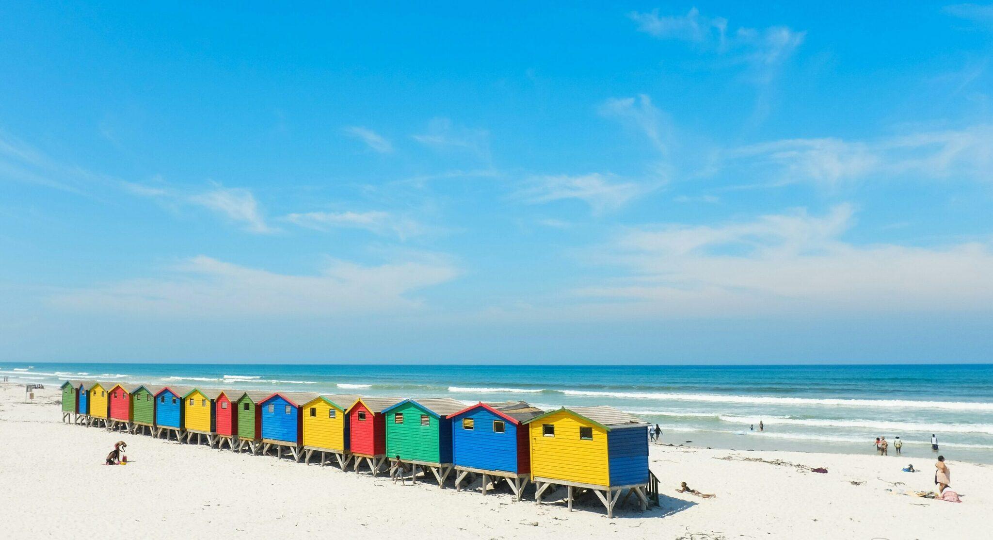 Une rangée de cabines de plage colorées alignées sur le sable blanc face à l’océan turquoise