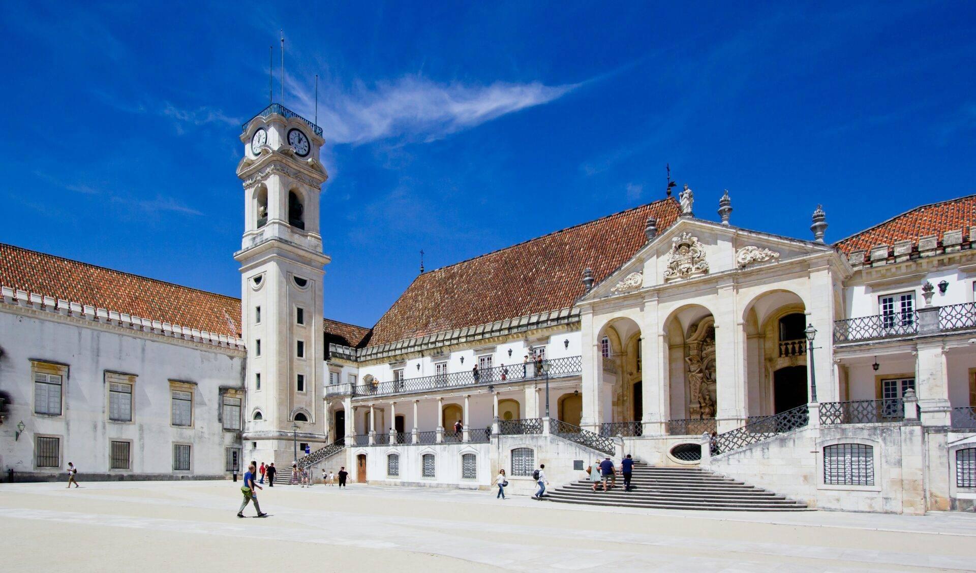 Cortile interno di un’università storica con campanile bianco, edifici coloniali e azulejos sotto un cielo azzurro