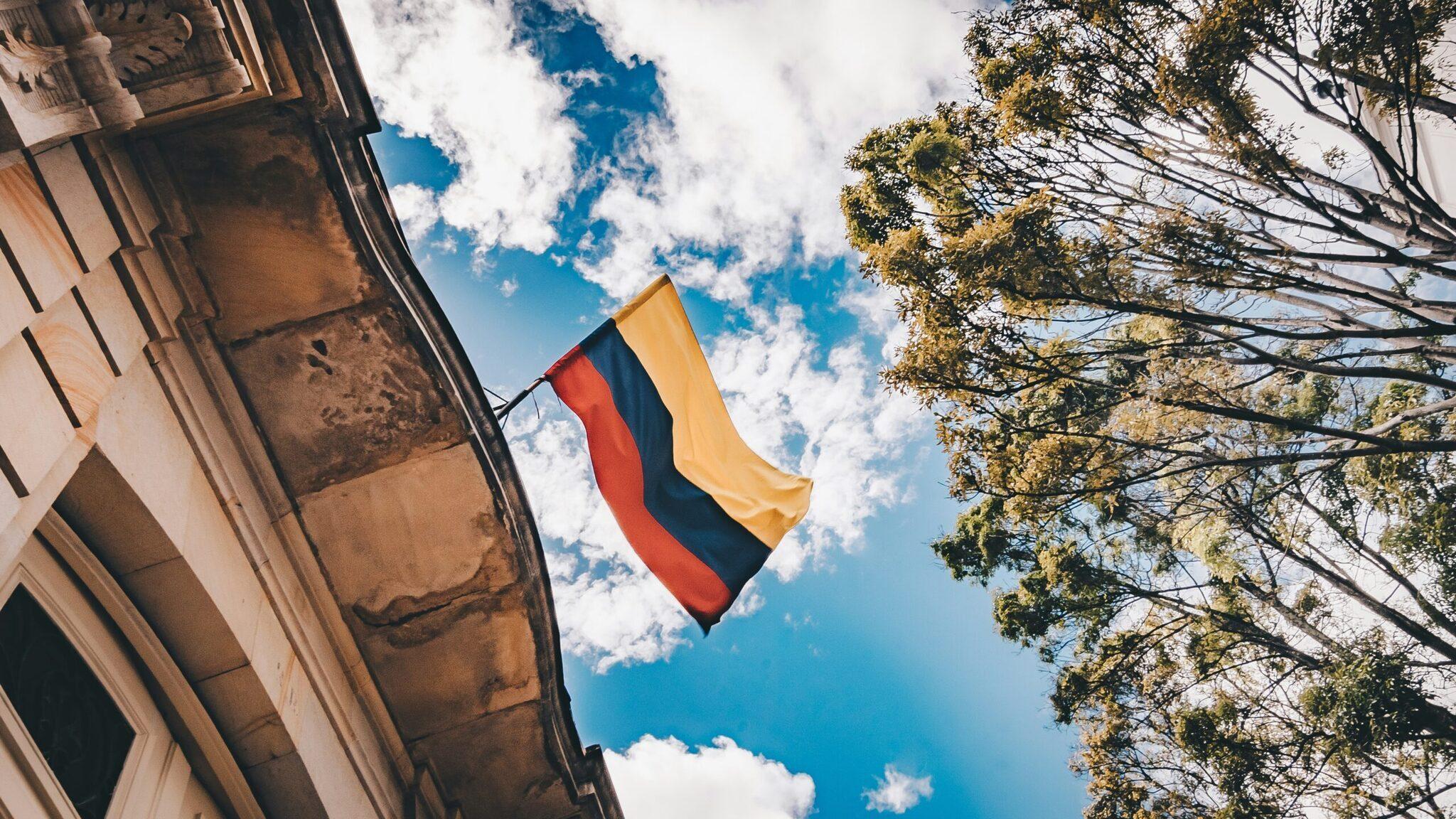 Drapeau colombien flottant au vent devant une façade coloniale sous un ciel bleu dégagé