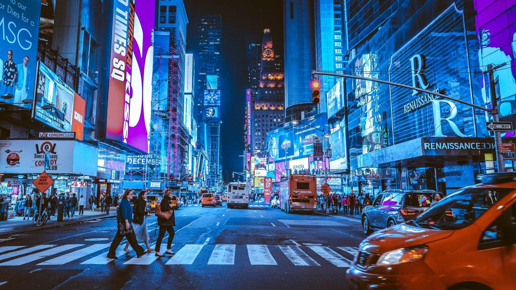 Une rue urbaine animée illuminée de publicités colorées avec des piétons traversant et des taxis oranges la nuit