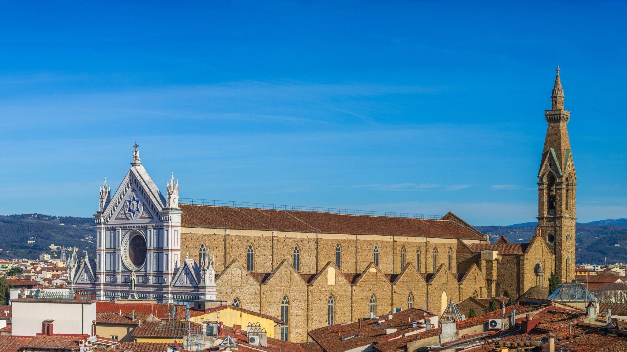 Vue panoramique sur Florence montrant une basilique en pierre ocre, un campanile élancé et le dôme blanc d’une cathédrale sous ciel bleu