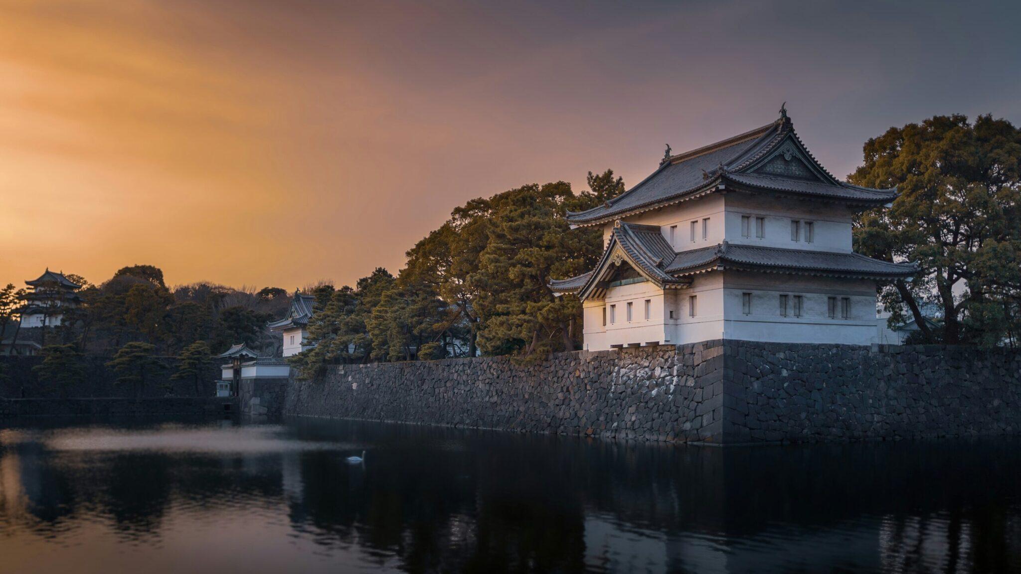 Un château japonais blanc aux toits en pagode se reflète dans un étang calme au crépuscule, entouré de verdure