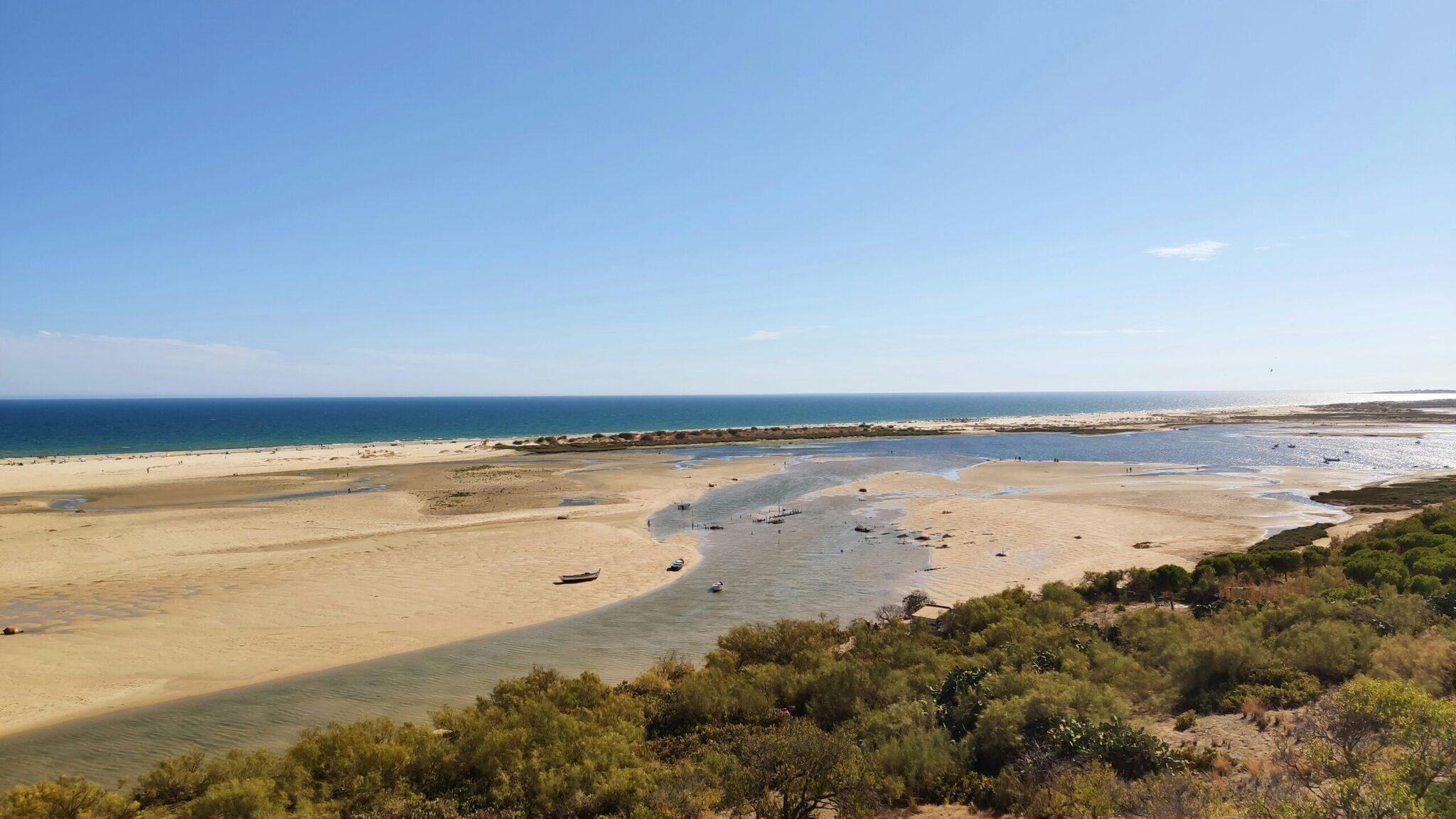 Luftaufnahme einer Küstenbucht mit Sandstrand, türkisblauem Wasser und vertäuten Booten bei schönem Wetter