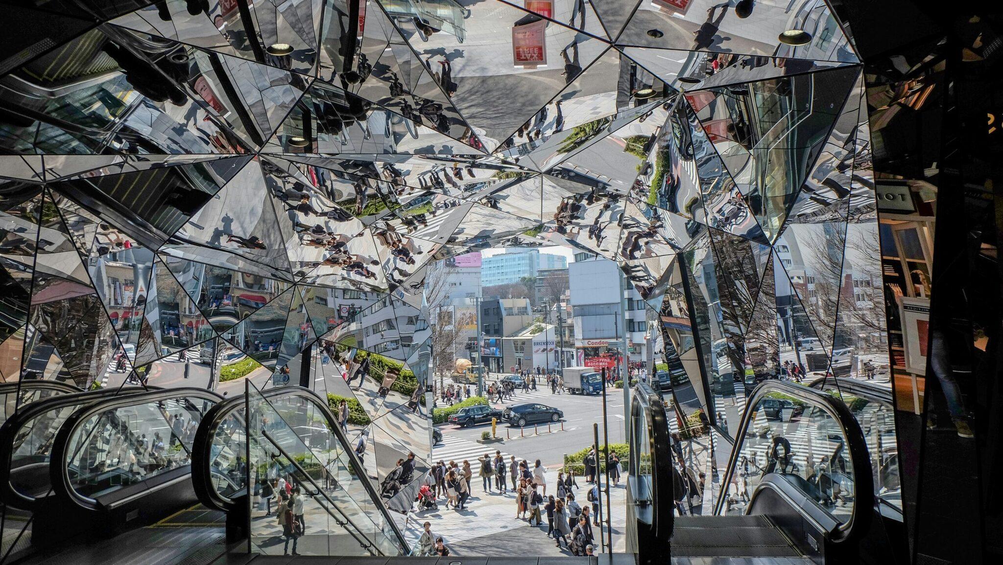 Vue depuis l’intérieur d’une galerie commerciale sur une place publique animée avec escaliers mécaniques et bâtiments urbains