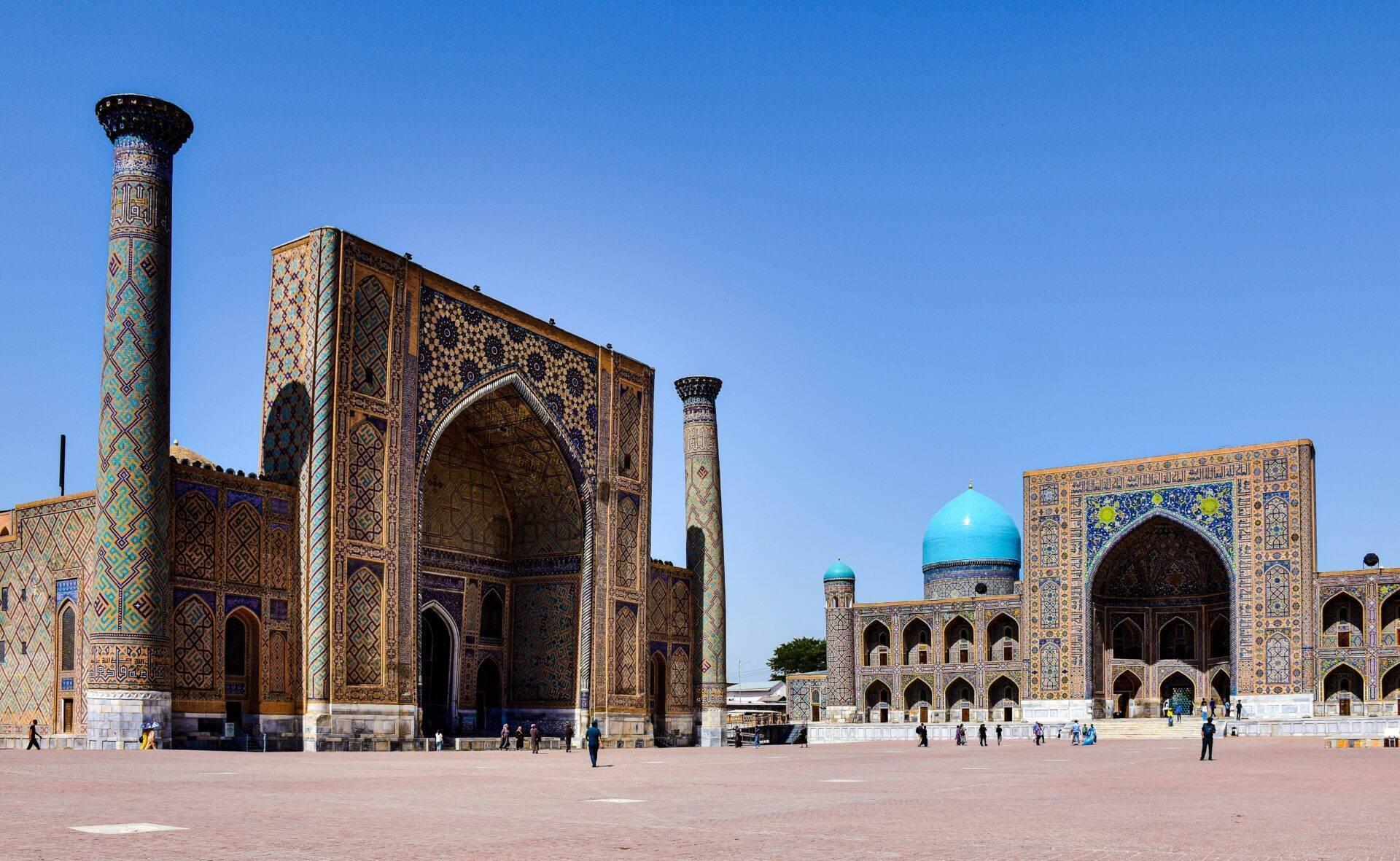 Grande place avec édifices islamiques richement décorés aux dômes turquoise et façades géométriques colorées