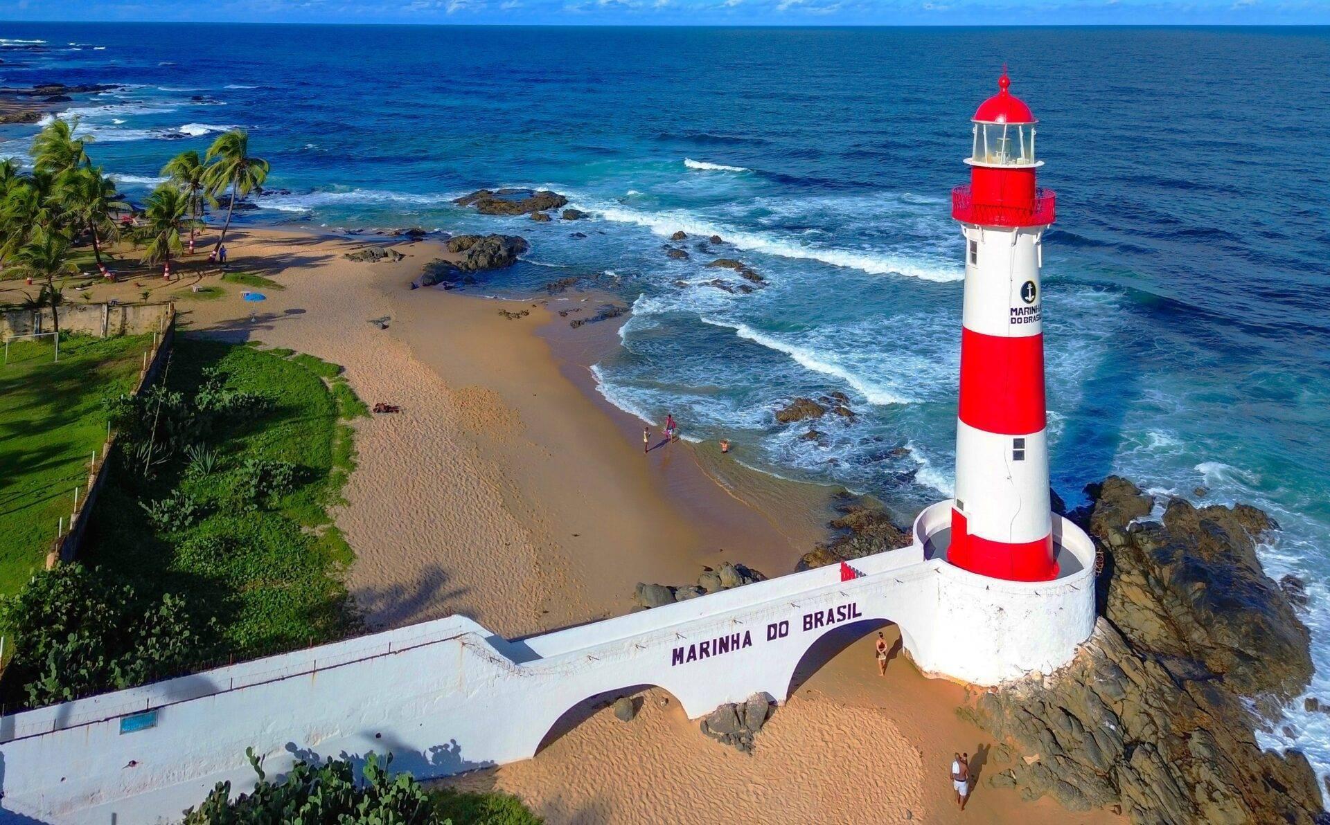 Faro rojo y blanco junto a la playa con palmeras, rocas y océano azul bajo un cielo despejado en Abaco