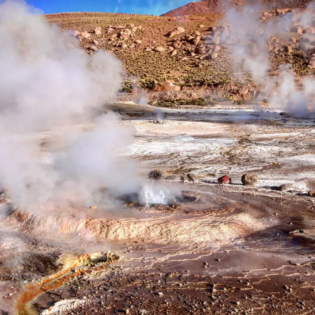 Geysers et sources chaudes fumantes dans un paysage désertique montagneux avec dépôts minéraux colorés