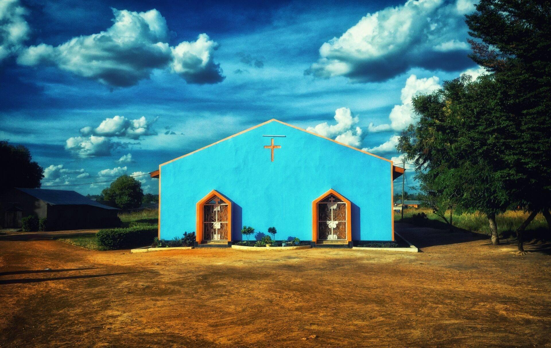 Eine Kirche mit leuchtend blauen Wänden und orangefarbenen Türen in der afrikanischen Savanne unter bewölktem Himmel