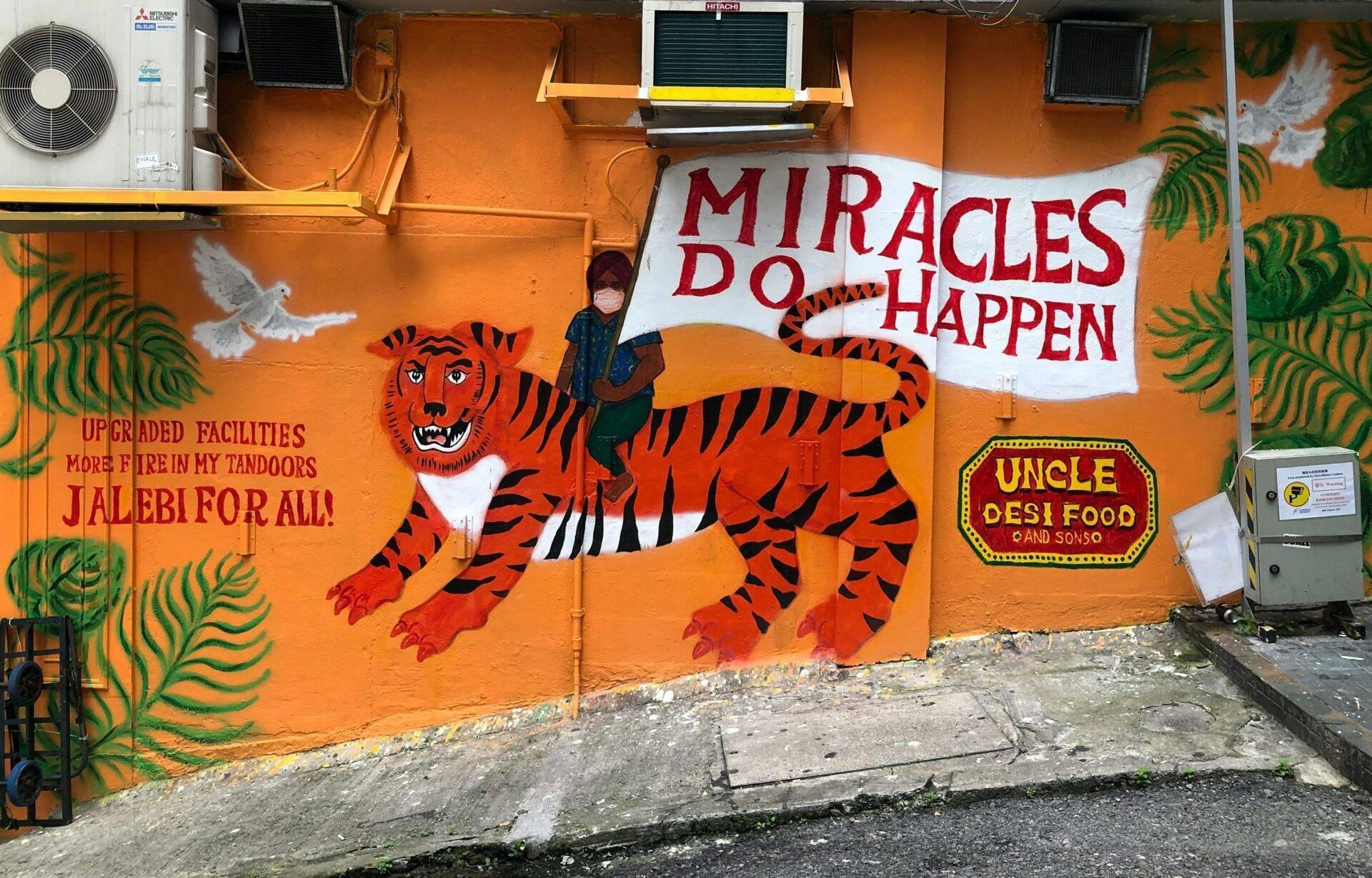 Façade orange colorée avec un tigre peint en rouge et noir, une femme posant devant, et des affiches de restaurants desi
