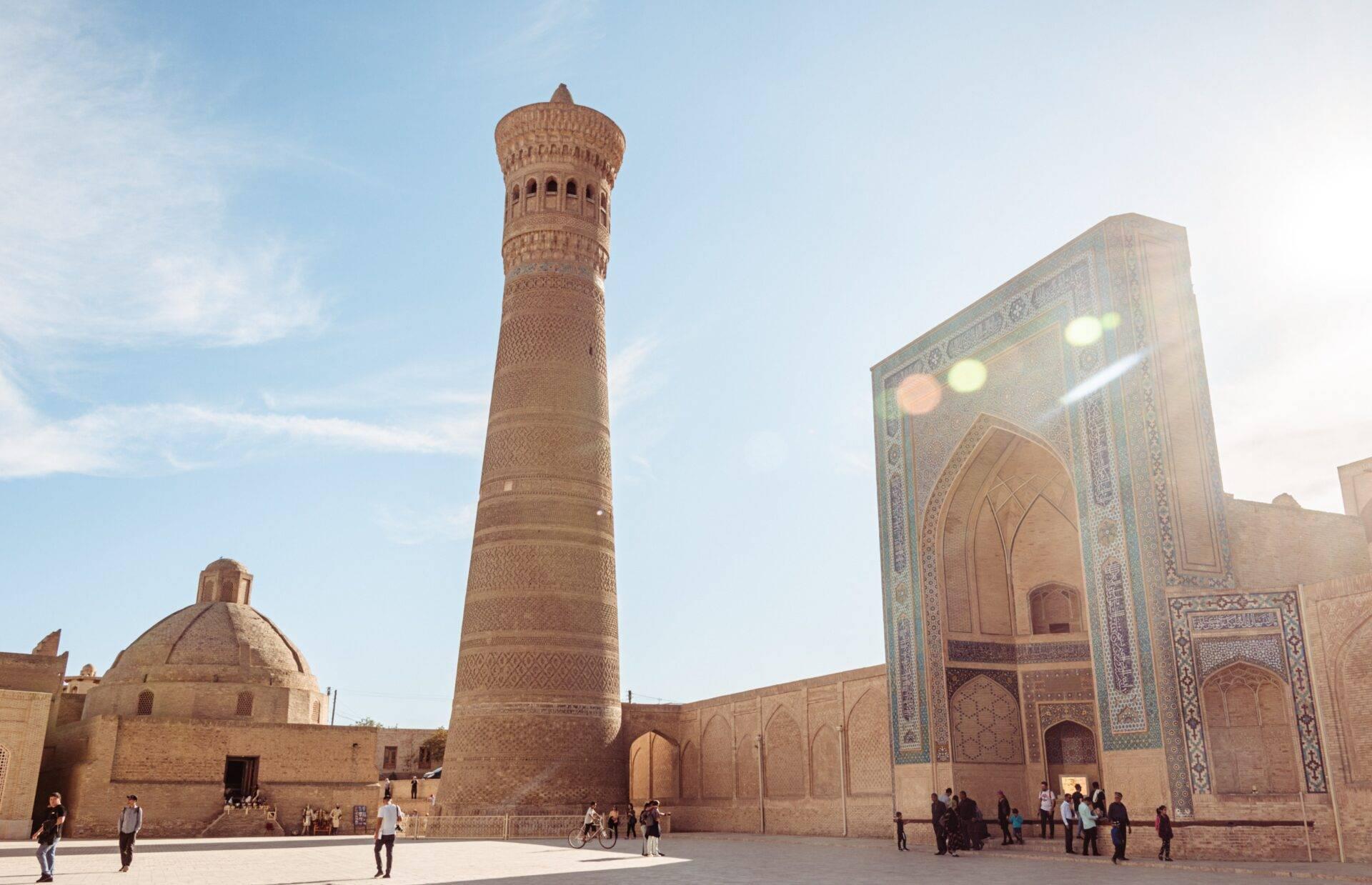Une cour de madrasah historique avec minaret en brique, portail monumental orné et visiteurs sous ciel dégagé