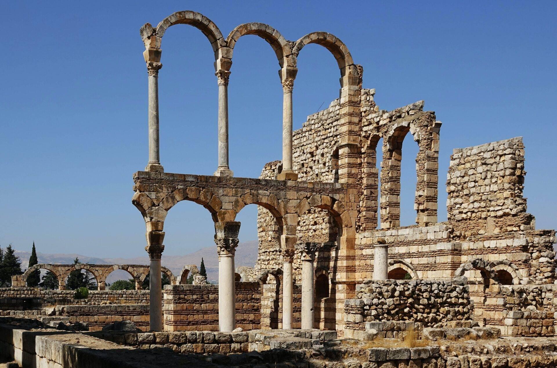 Ruines romaines antiques avec colonnes et arches en pierre sous un ciel dégagé, montagne en arrière-plan