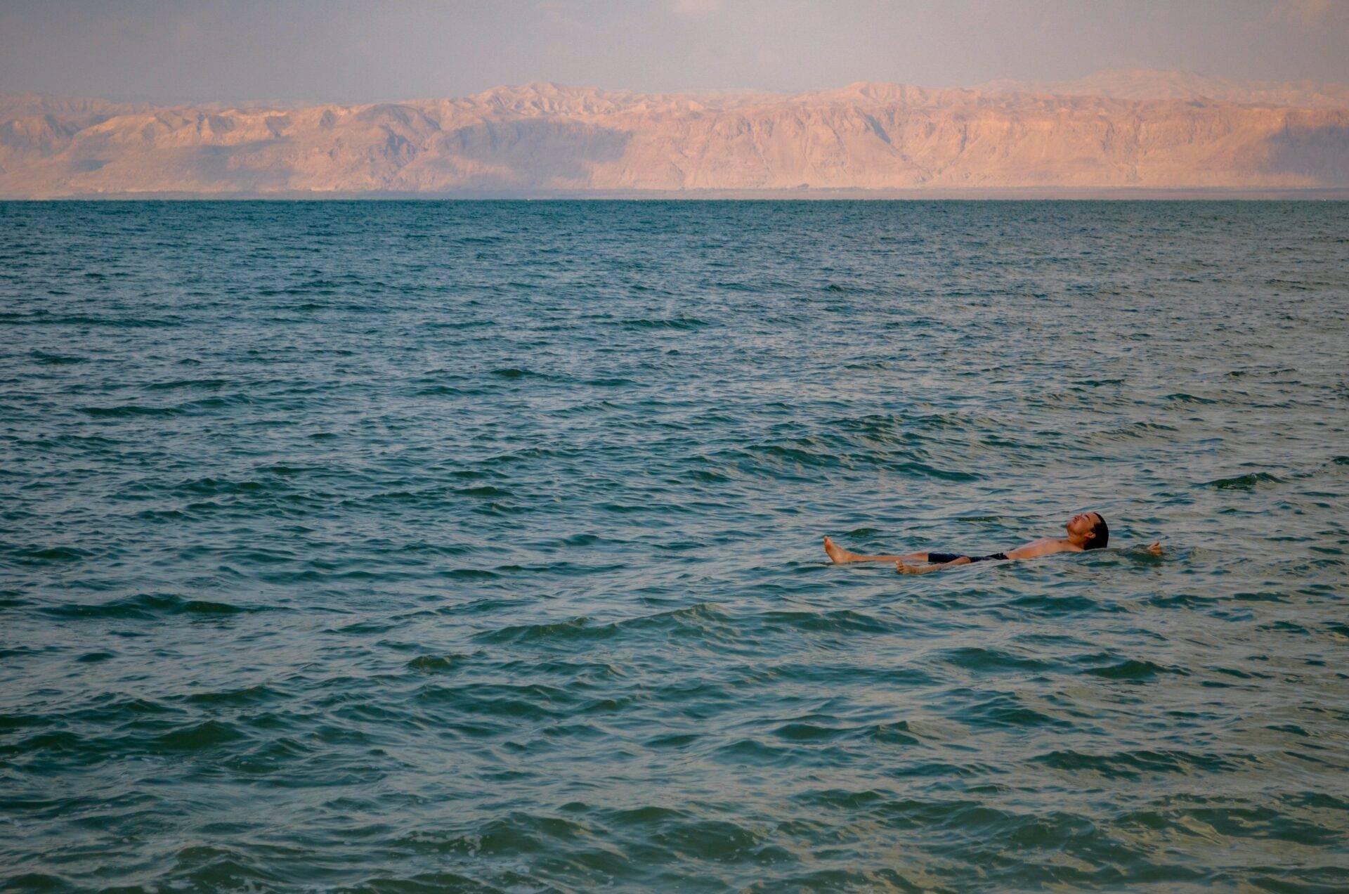 Un uomo galleggia senza sforzo in un mare turchese di fronte a maestose scogliere desertiche color ocra