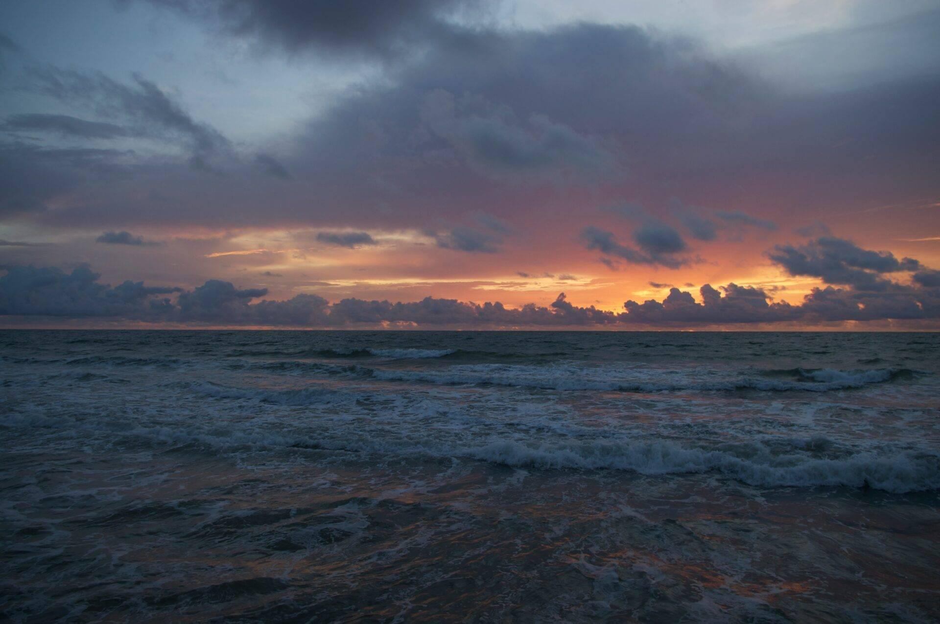 Tramonto spettacolare sull’oceano con nuvole dorate e onde che si infrangono su una spiaggia deserta