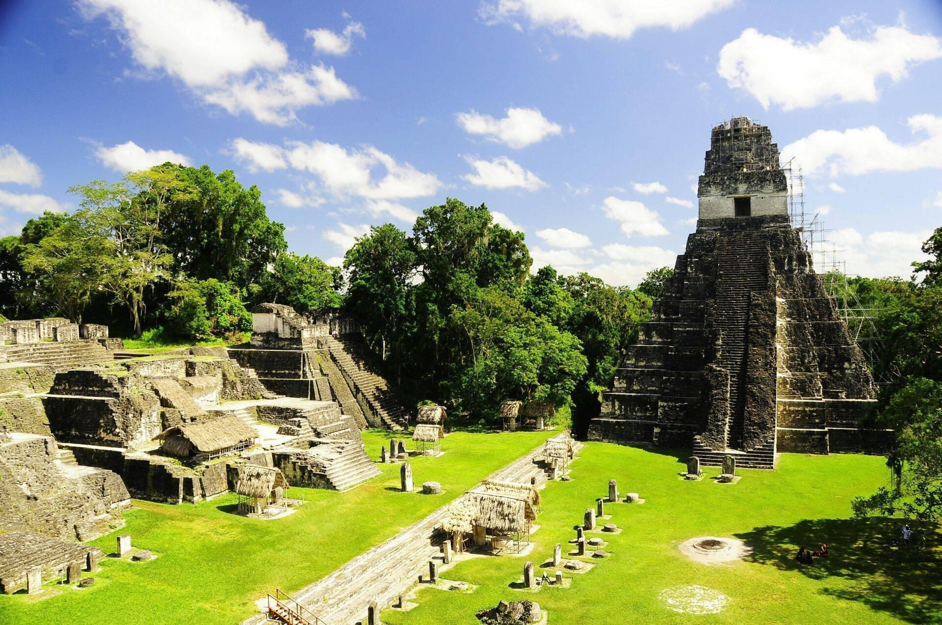 Ruines mayas antiques avec pyramide centrale, structures en pierre et végétation tropicale luxuriante sous ciel bleu