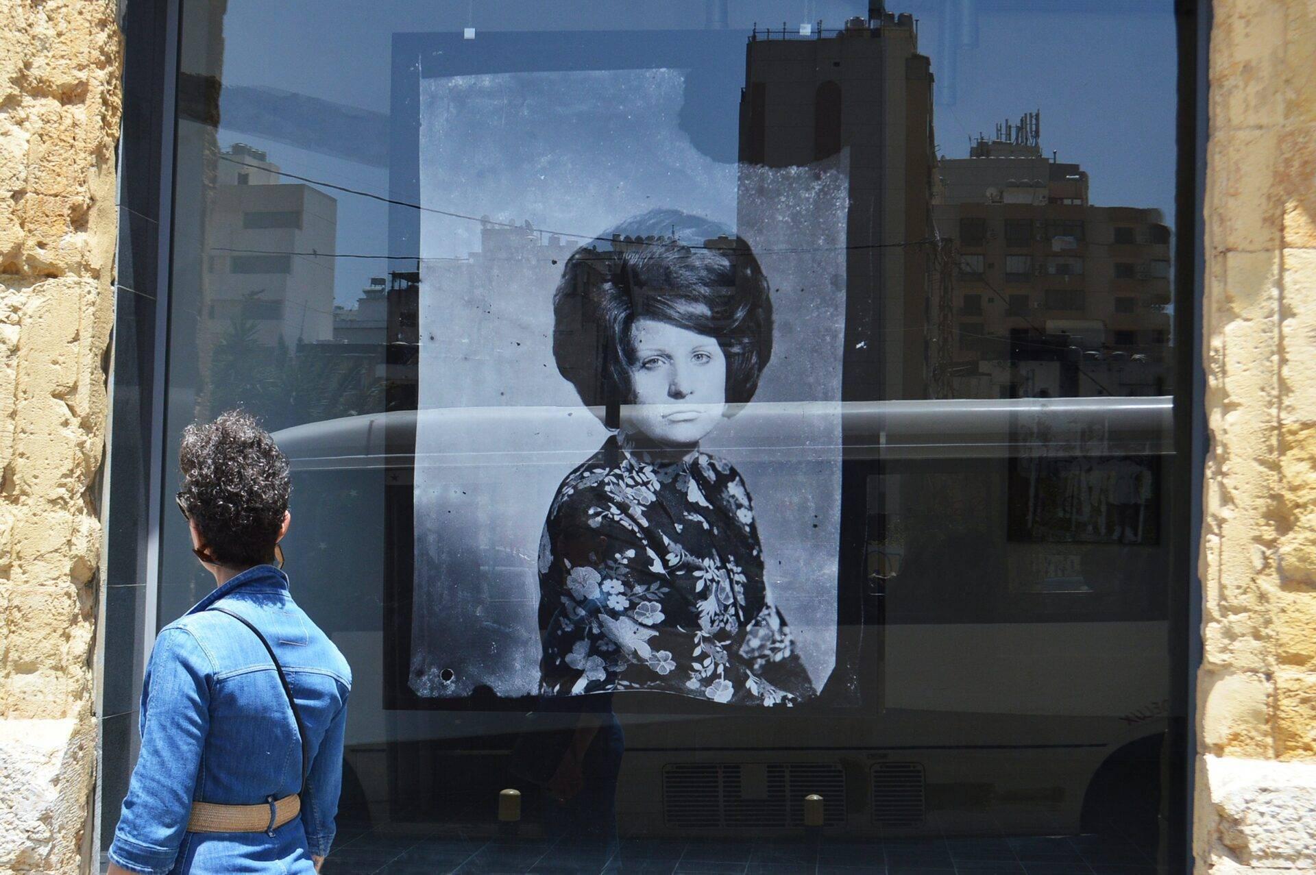 Une femme observe un portrait en noir et blanc d’une femme des années 1960 affiché sur une vitre en milieu urbain