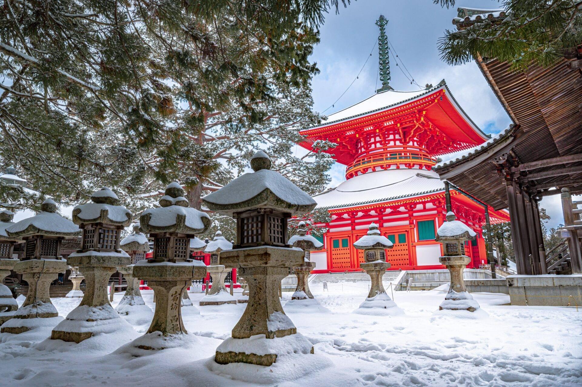 Un temple bouddhiste japonais aux toits rouges éclatants entouré de lanternes en pierre enneigées sous les arbres givrés