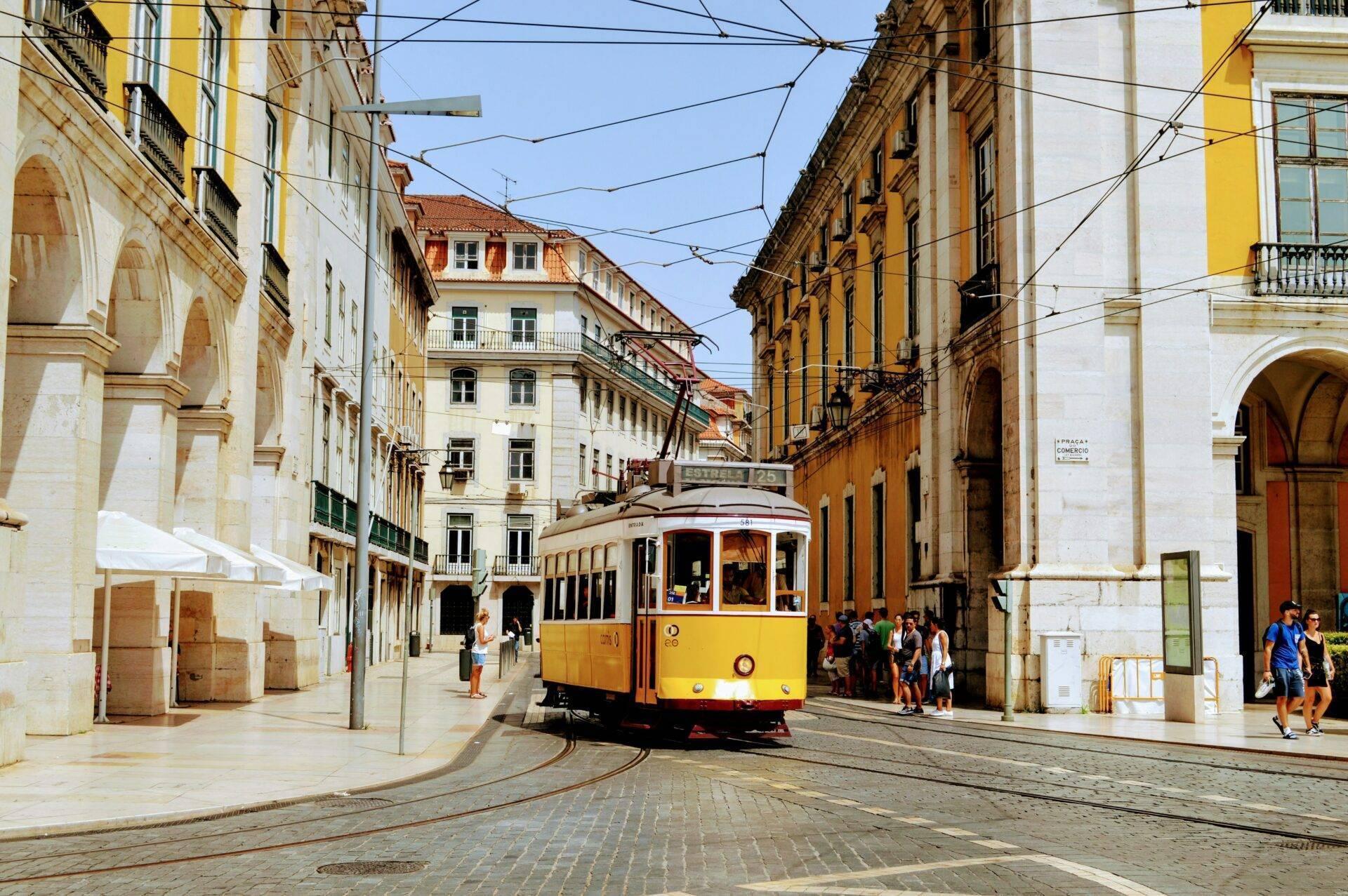 Un tramway jaune et rouge circule dans une rue pavée d’une ville historique européenne bordée d’élégants immeubles anciens