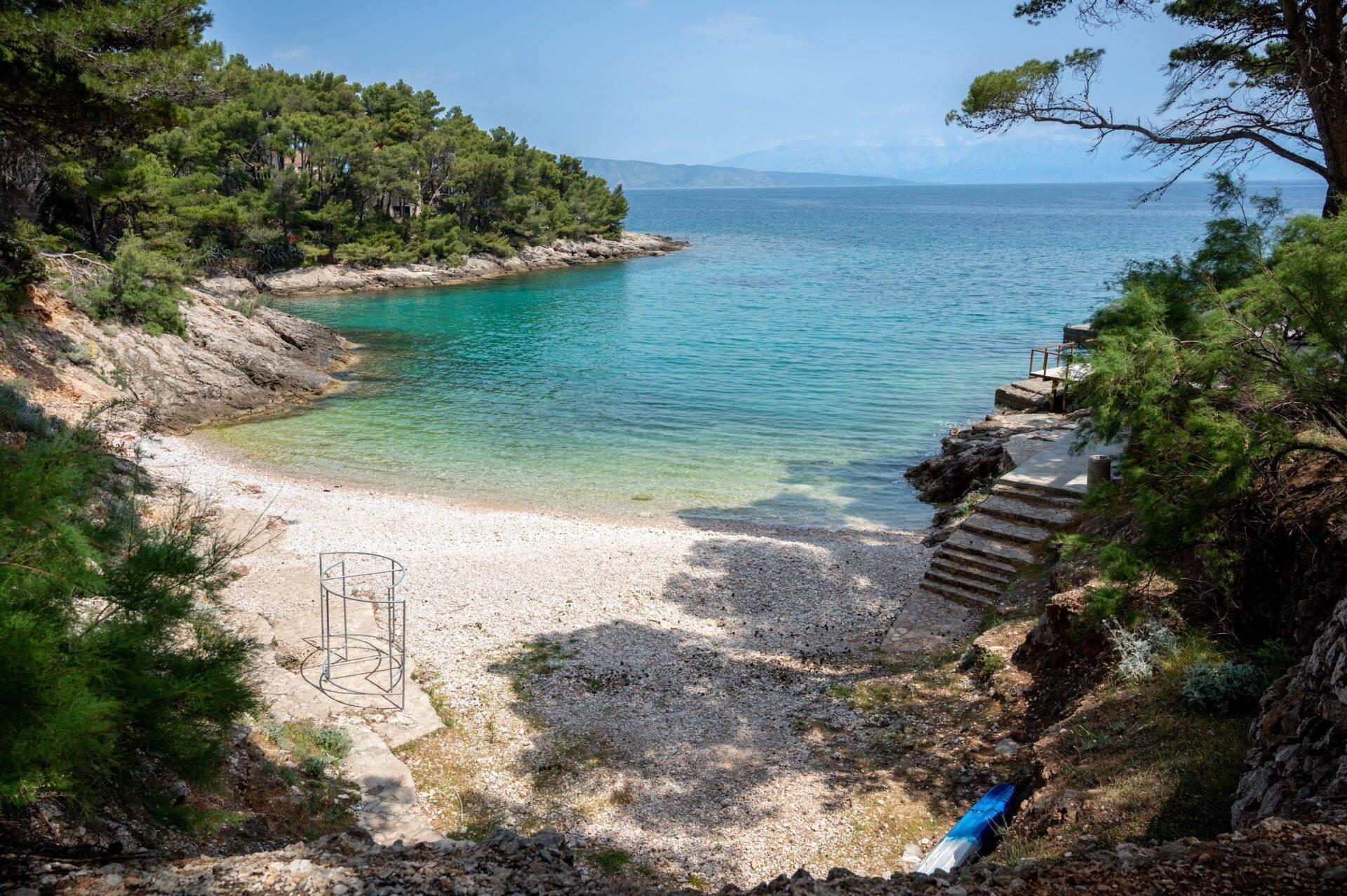 Kleine mediterrane Bucht mit Kieselstrand, türkisfarbenem Wasser und bewaldeten Felsklippen in Kroatien