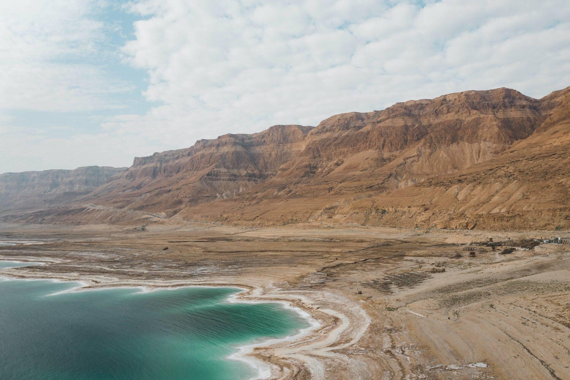 Vista aerea di un mare turchese con rive minerali bianche, incorniciato da scogliere rocciose desertiche ocra e brune