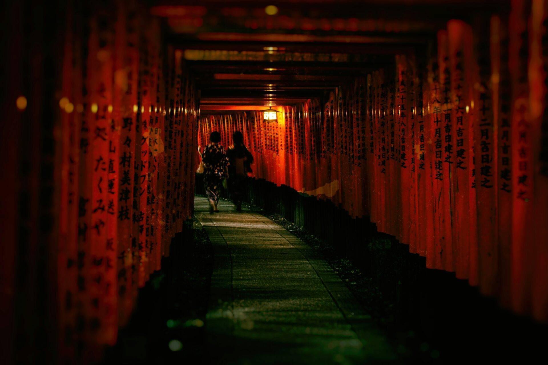 Tunnel de portiques torii rouges illuminés la nuit avec des visiteurs marchant dans une allée au Japon