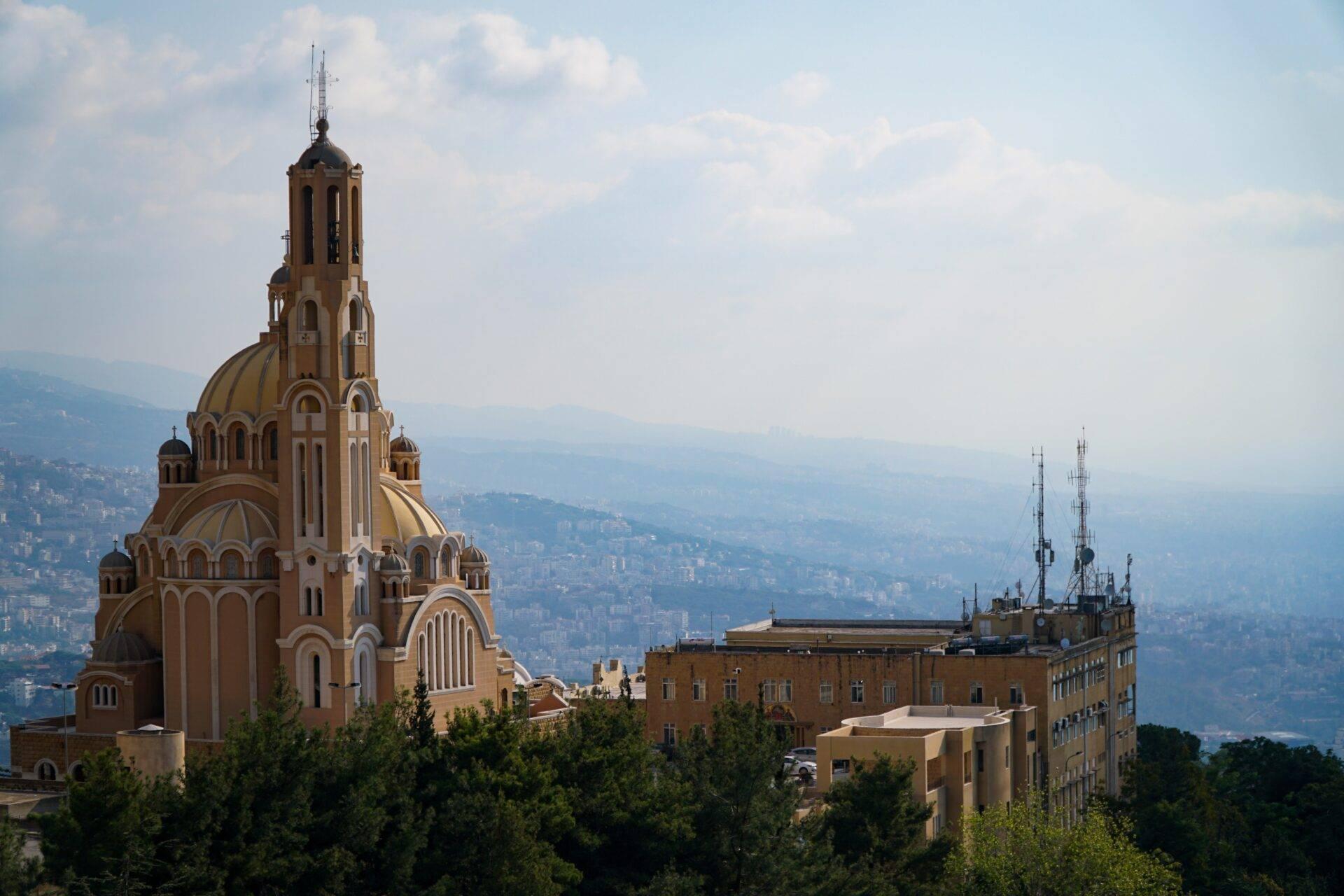 Église orthodoxe dorée sur une montagne libanaise surplombant une vallée habitée sous un ciel dégagé