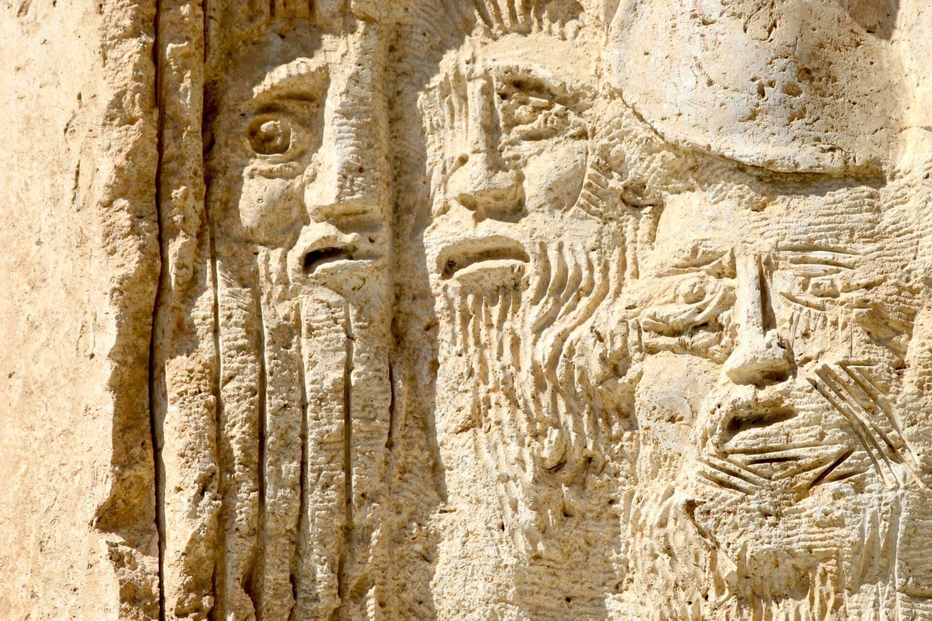 Bassorilievo in pietra calcarea che raffigura figure umane e iscrizioni antiche incise sulla facciata di un tempio storico