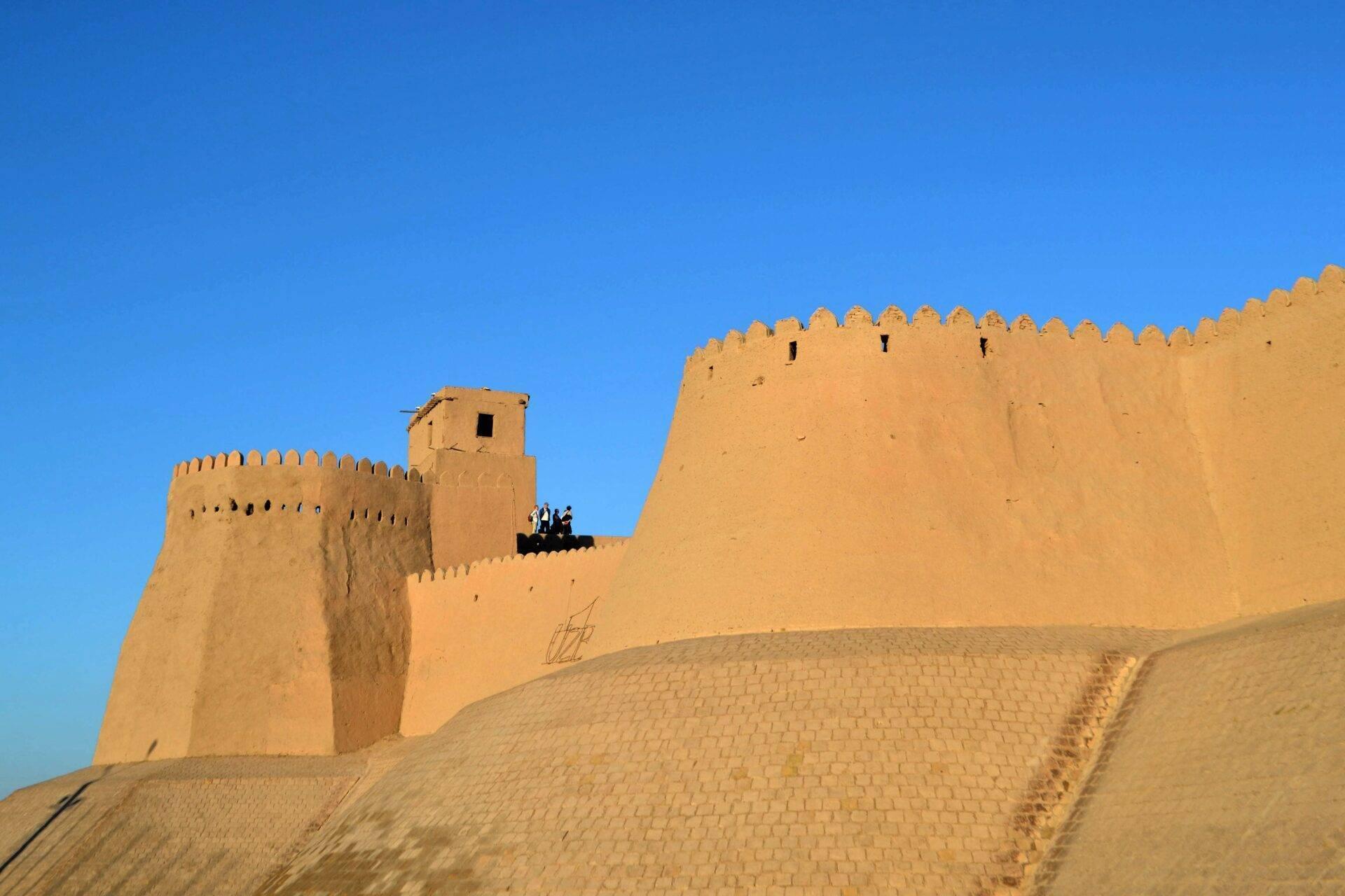 Une forteresse historique en adobe beige aux remparts crénelés sous un ciel bleu dégagé