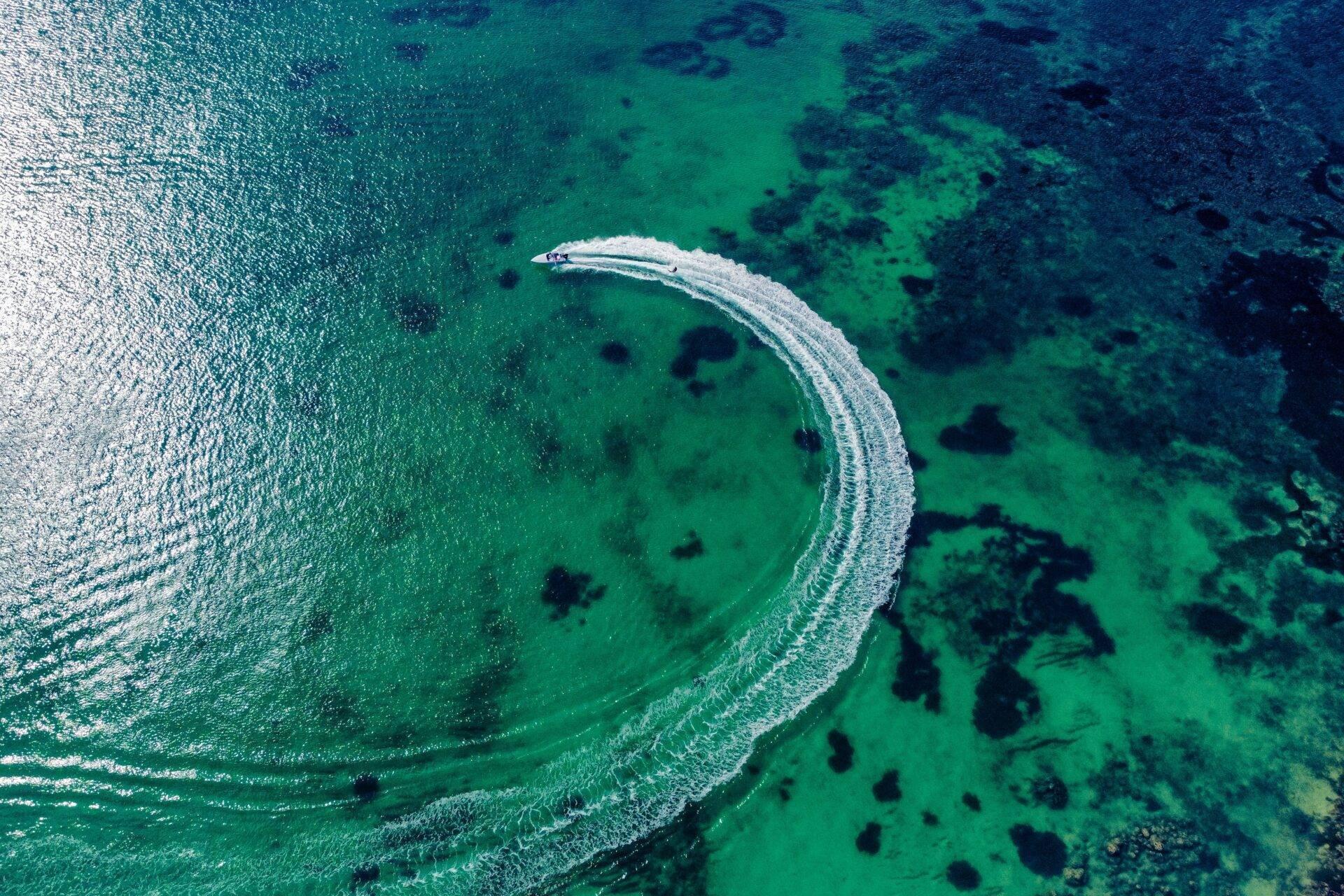 Ein Motorboot zieht eine weiße Kreisbahn auf kristallklarem türkisem Wasser, durchsetzt von schwarzen Felsen