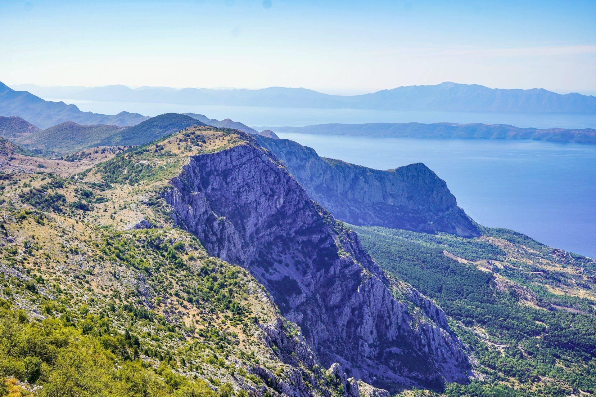 Panoramaansicht auf steile Kalksteinberge, die das türkisfarbene Mittelmeer und ferne Inseln überragen