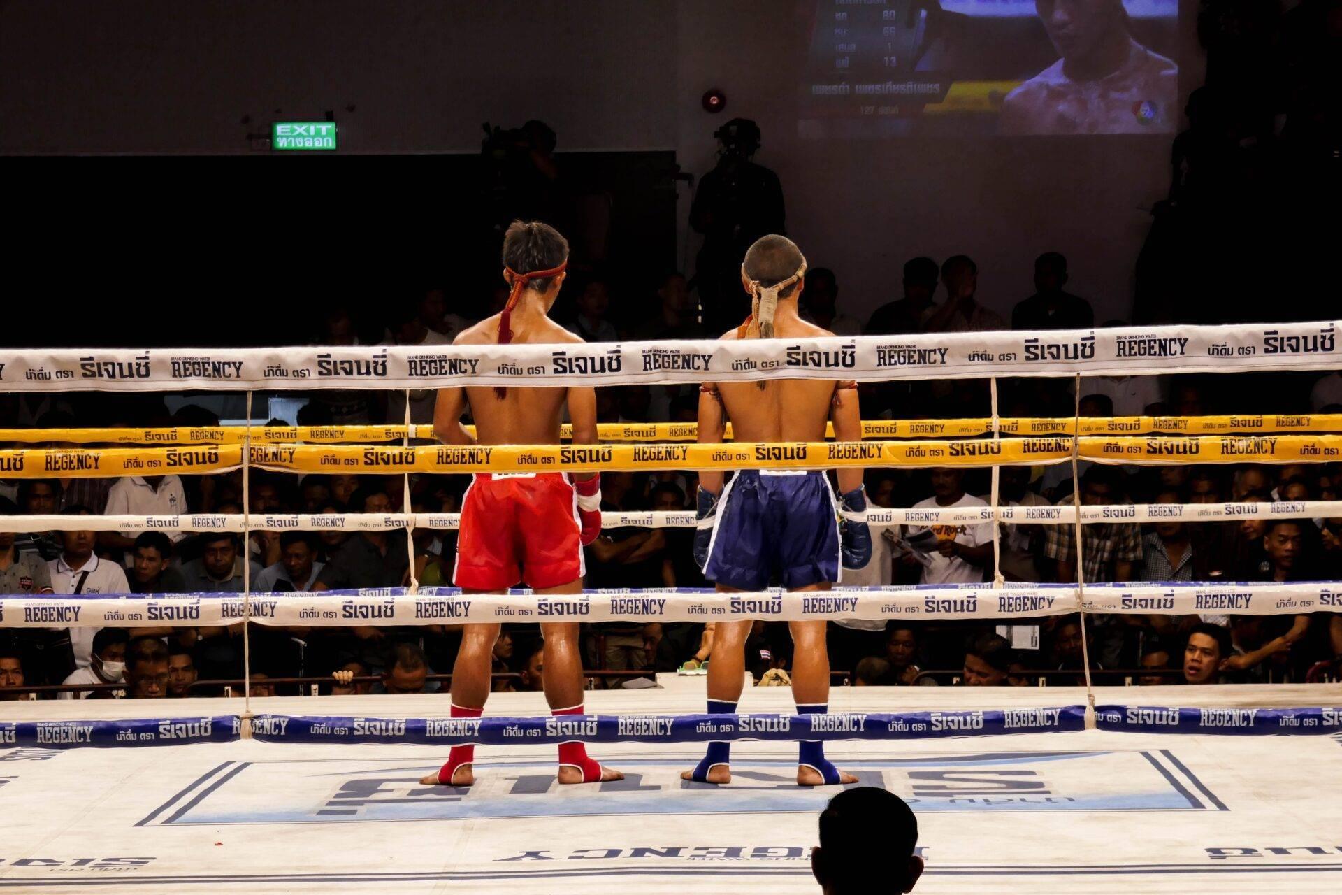 Deux boxeurs en ring lors d’un combat de boxe thaïlandaise dans une arène bondée de spectateurs