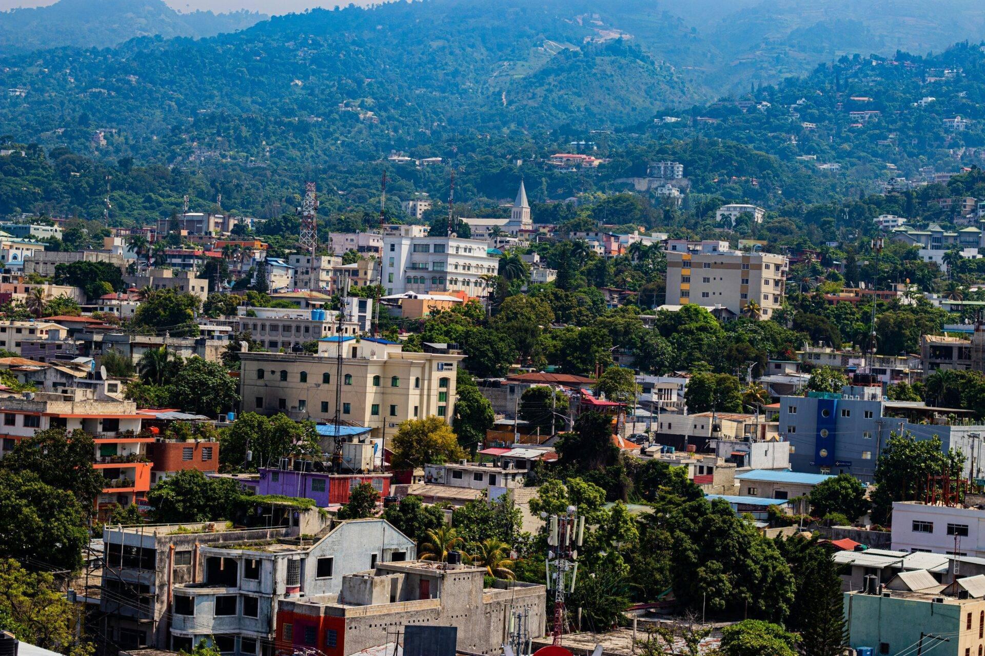 Vista aerea di una città tropicale montuosa con edifici colorati, vegetazione fitta e chiesa bianca al centro