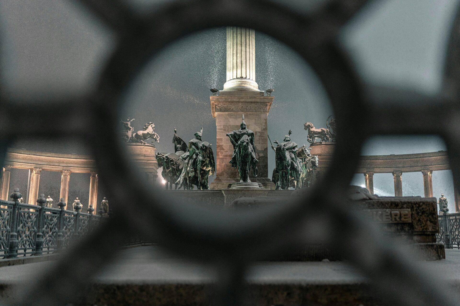 Vista attraverso una cancellata in ferro del monumento agli eroi con statue equestri e colonnata a Budapest
