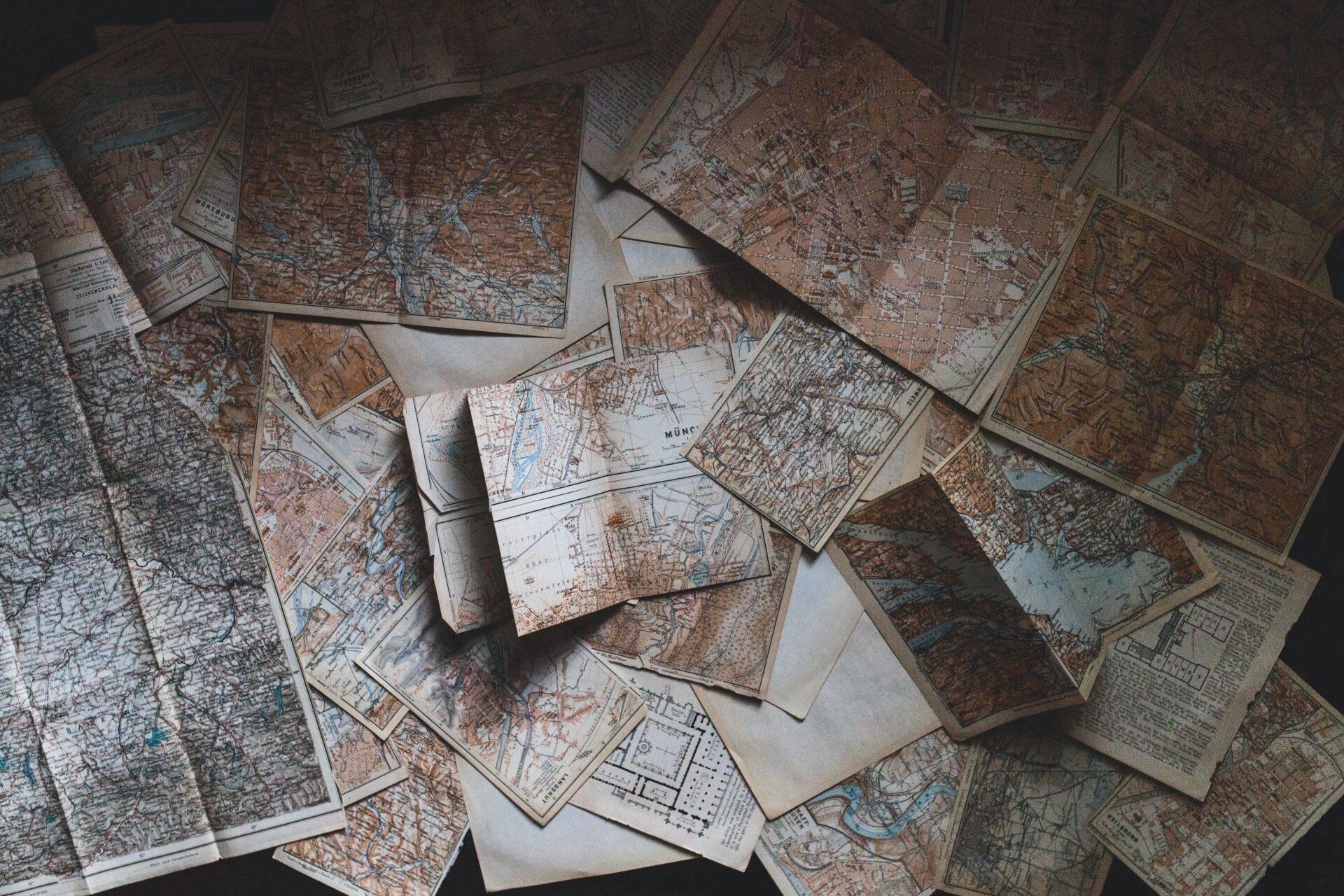 Collection de cartes géographiques anciennes et plans de villes étalés sur une surface blanche, évoquant la préparation d’un voyage