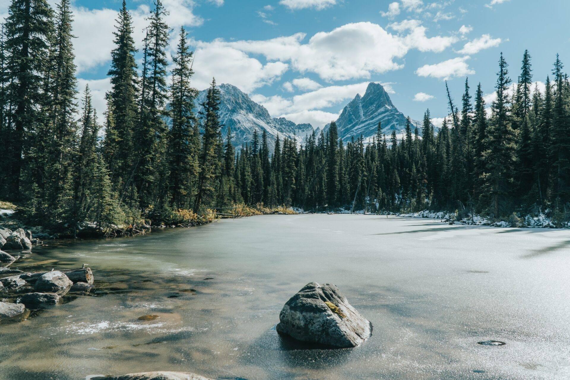 Un lac de montagne gelé entouré de forêts de conifères et de pics rocheux sous un ciel bleu dégagé