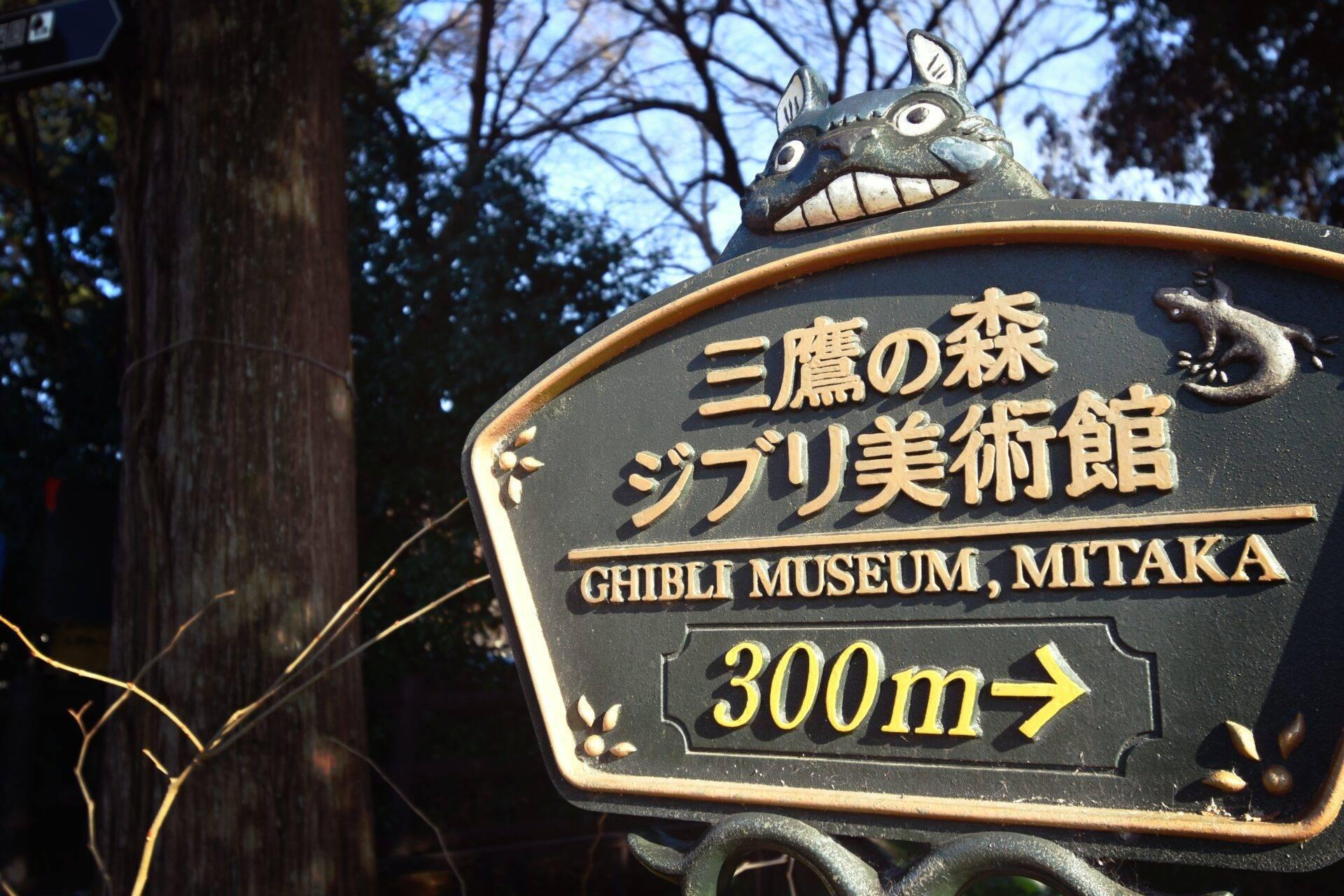 Panneau directif vers le Ghibli Museum Mitaka orné d’une créature fantastique, au cœur d’une forêt japonaise
