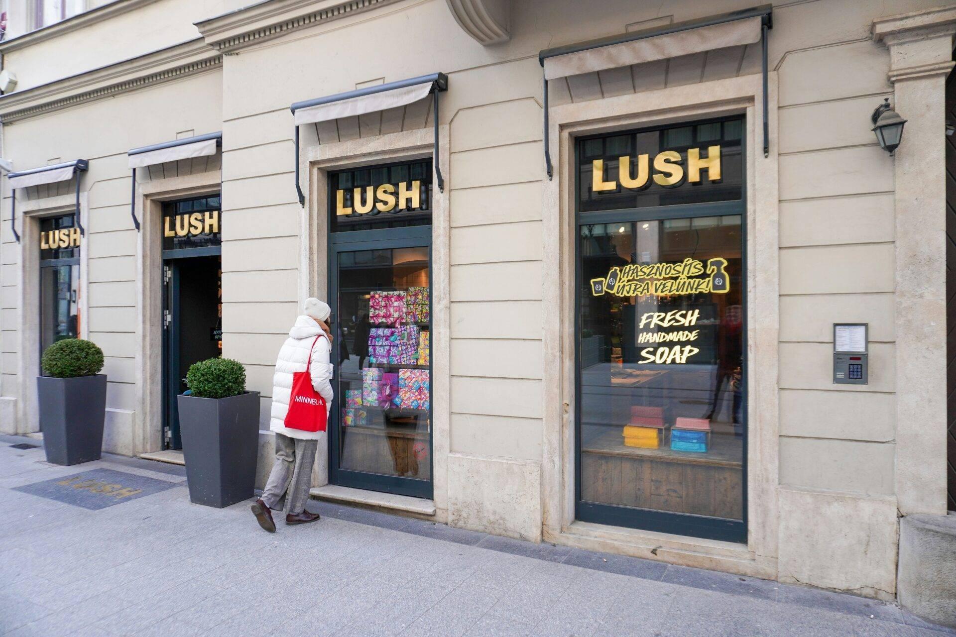 Una donna davanti a un negozio di cosmetici artigianali in una strada acciottolata europea con facciata classica